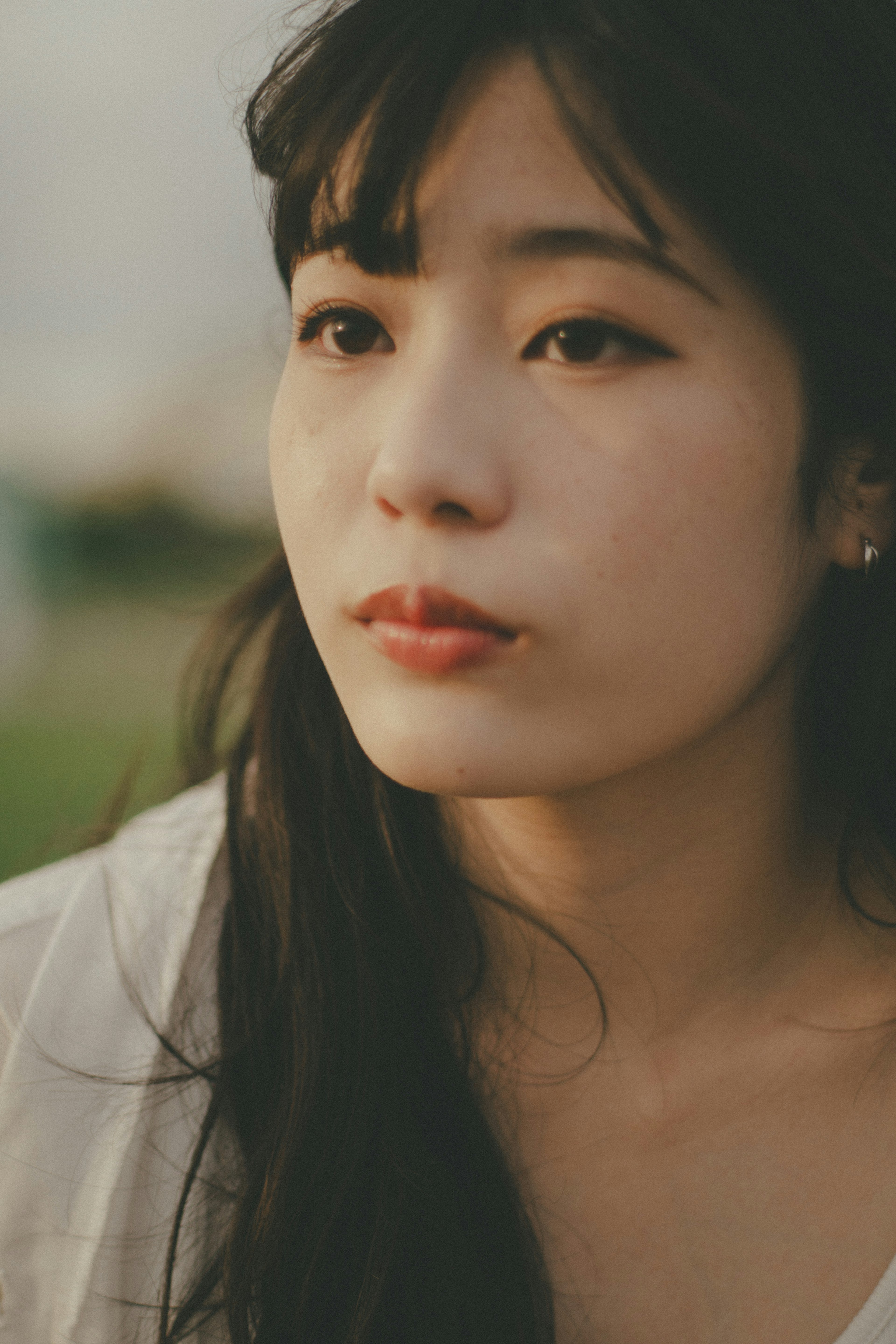 A woman with a serene expression sitting outdoors in natural light