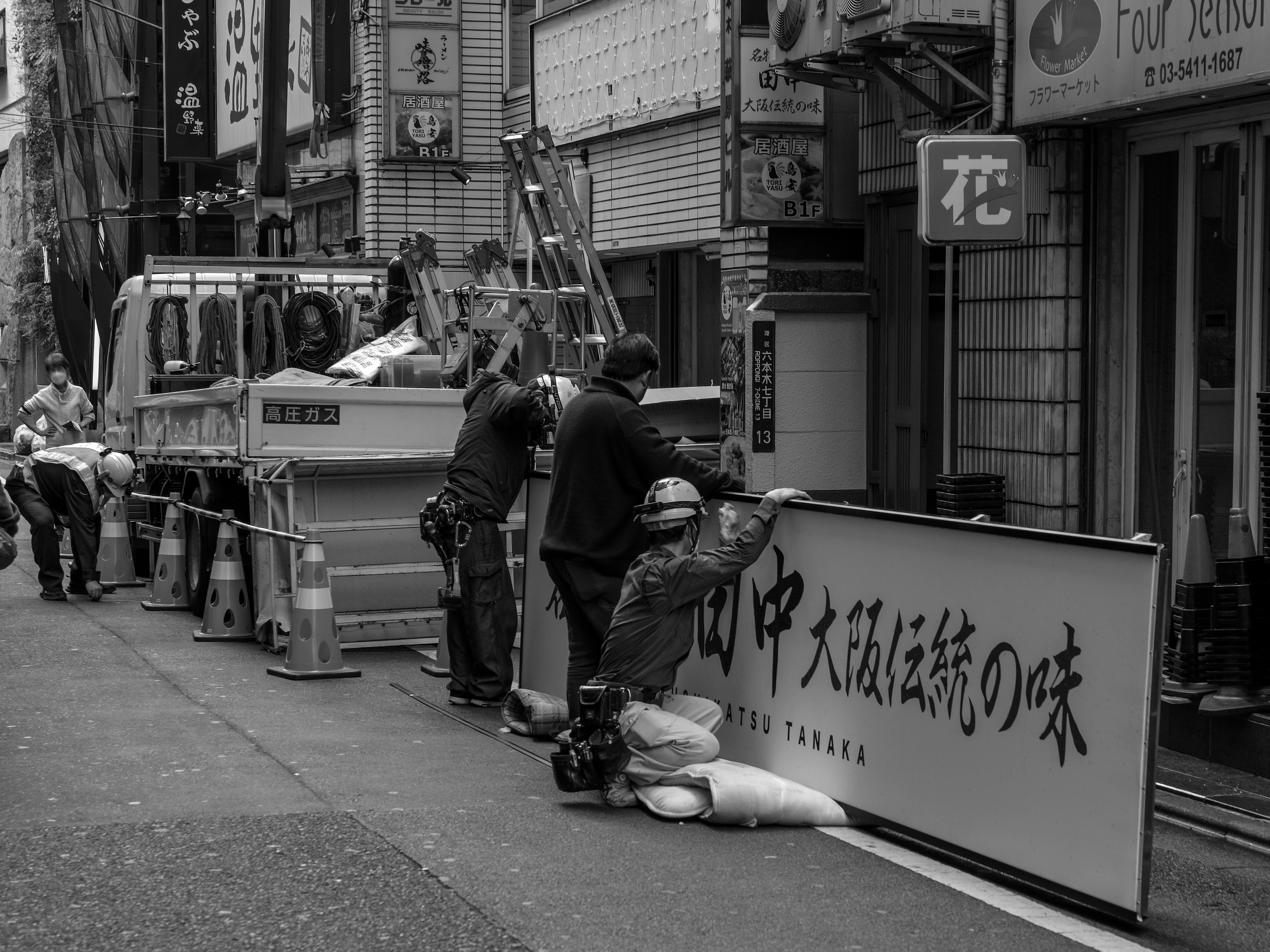 Des travailleurs et un véhicule de construction dans une scène de rue en noir et blanc