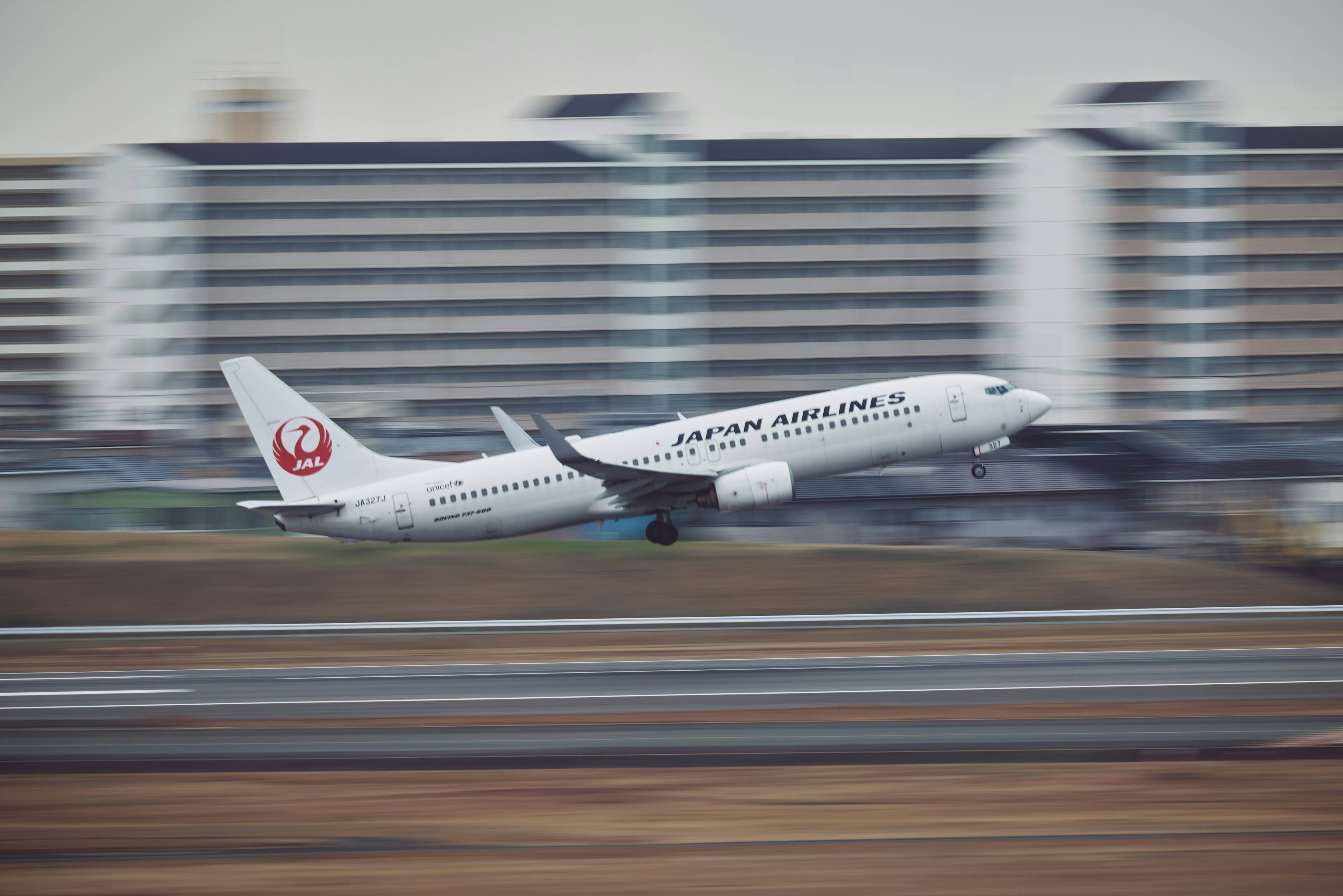 白い航空機が滑走路から離陸している様子 背景には高層ビルが見える