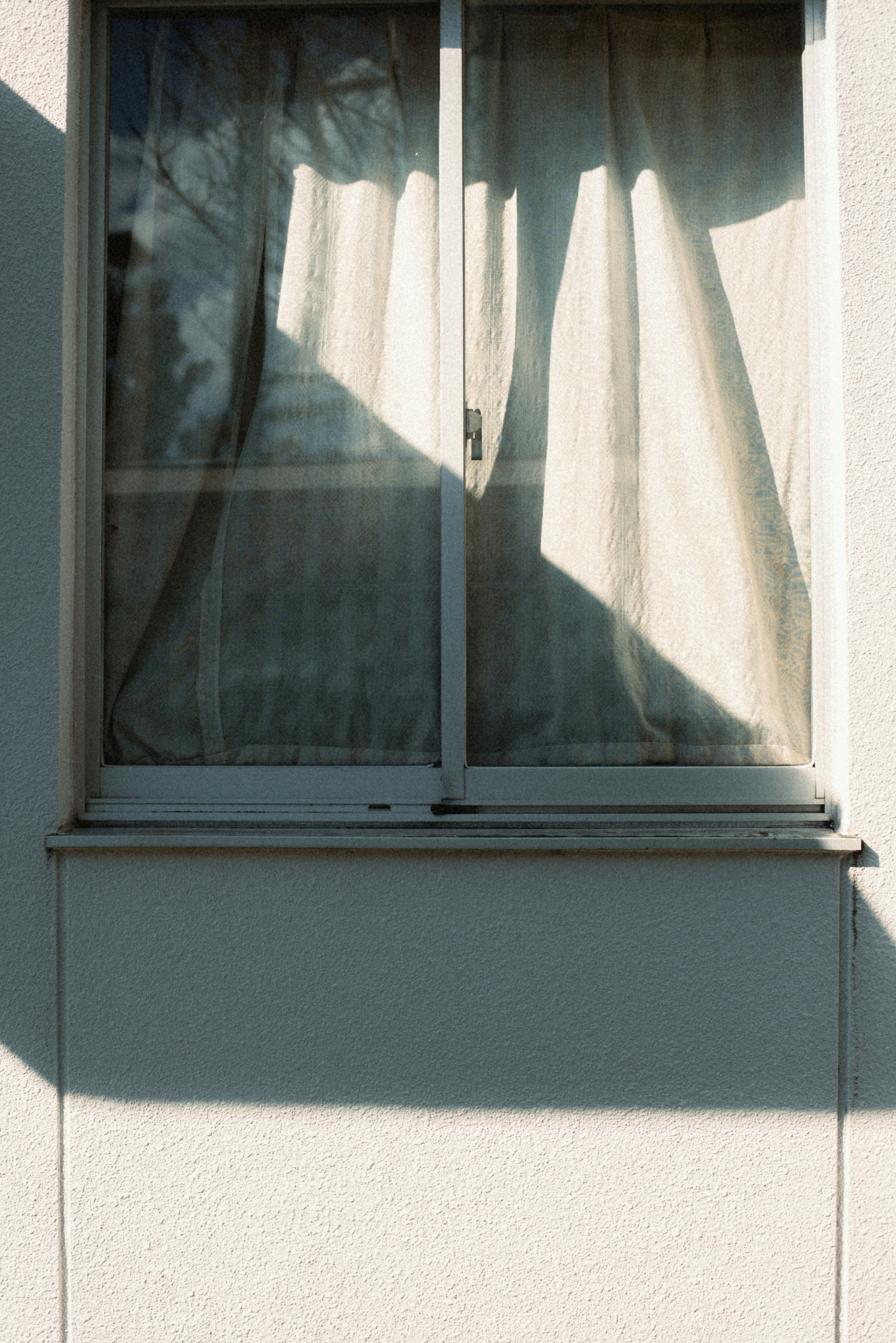 A simple exterior view of a window with curtains casting shadows