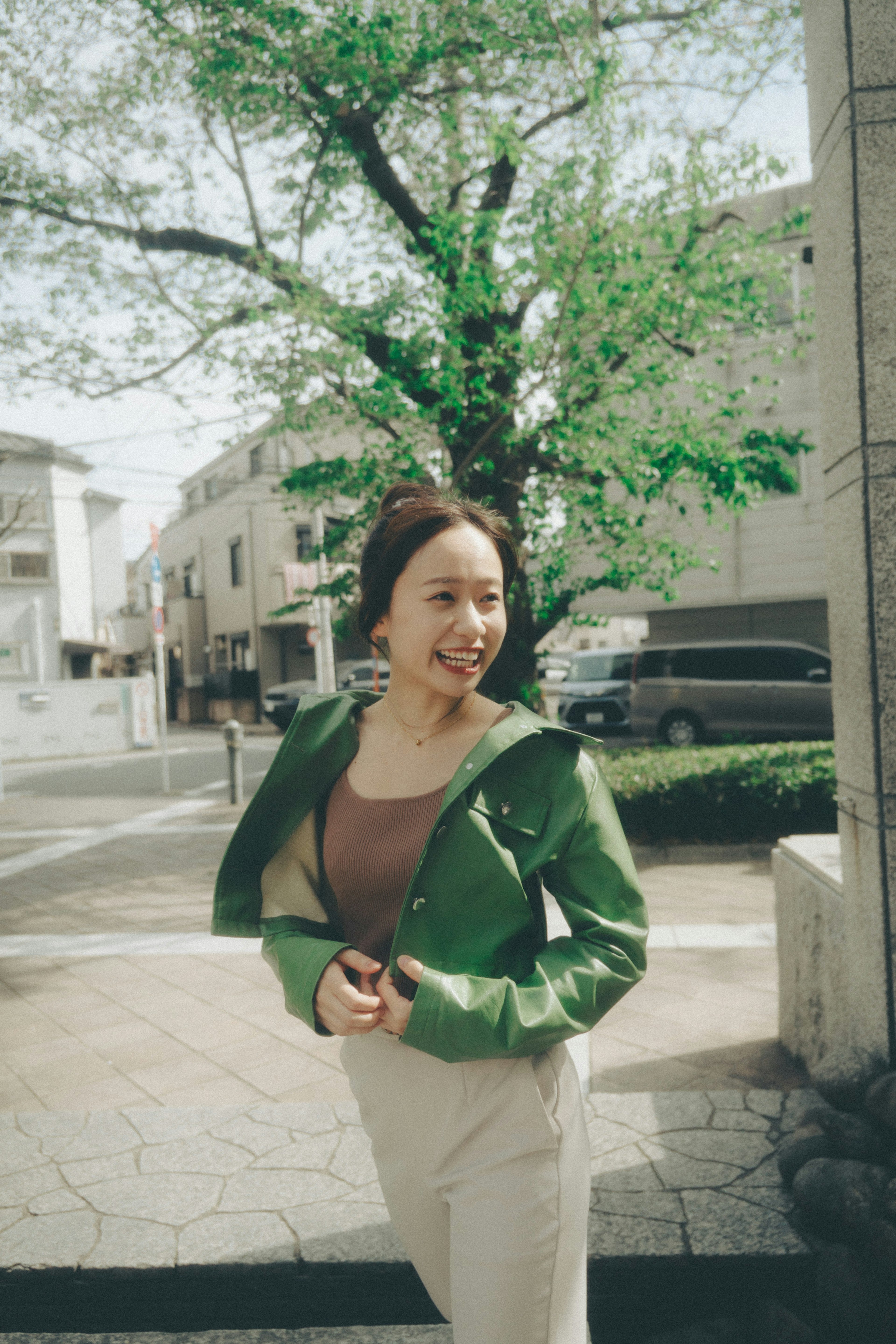 Mujer con chaqueta verde sonriendo en una esquina de la calle