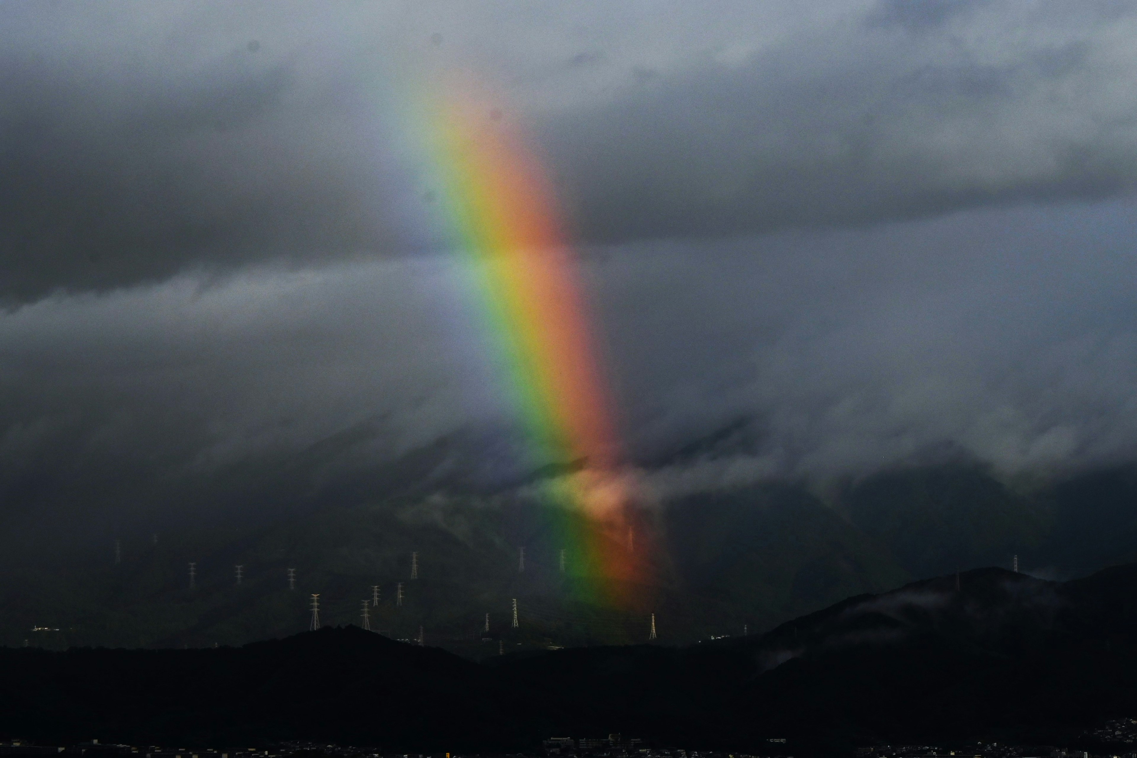 A vibrant rainbow emerging through dark clouds illuminating the landscape