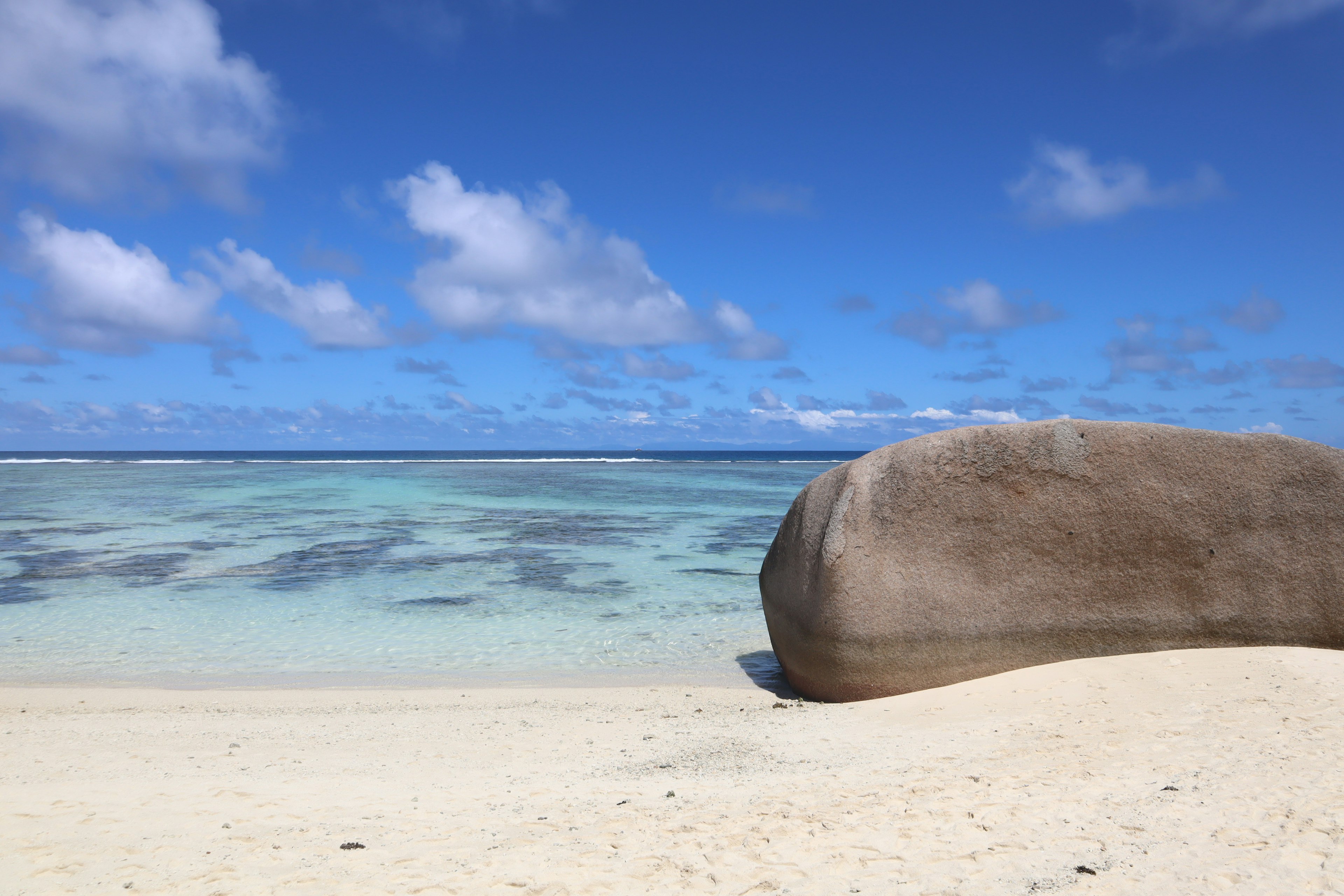 Una grande roccia su una spiaggia di sabbia sotto un cielo blu con acqua chiara