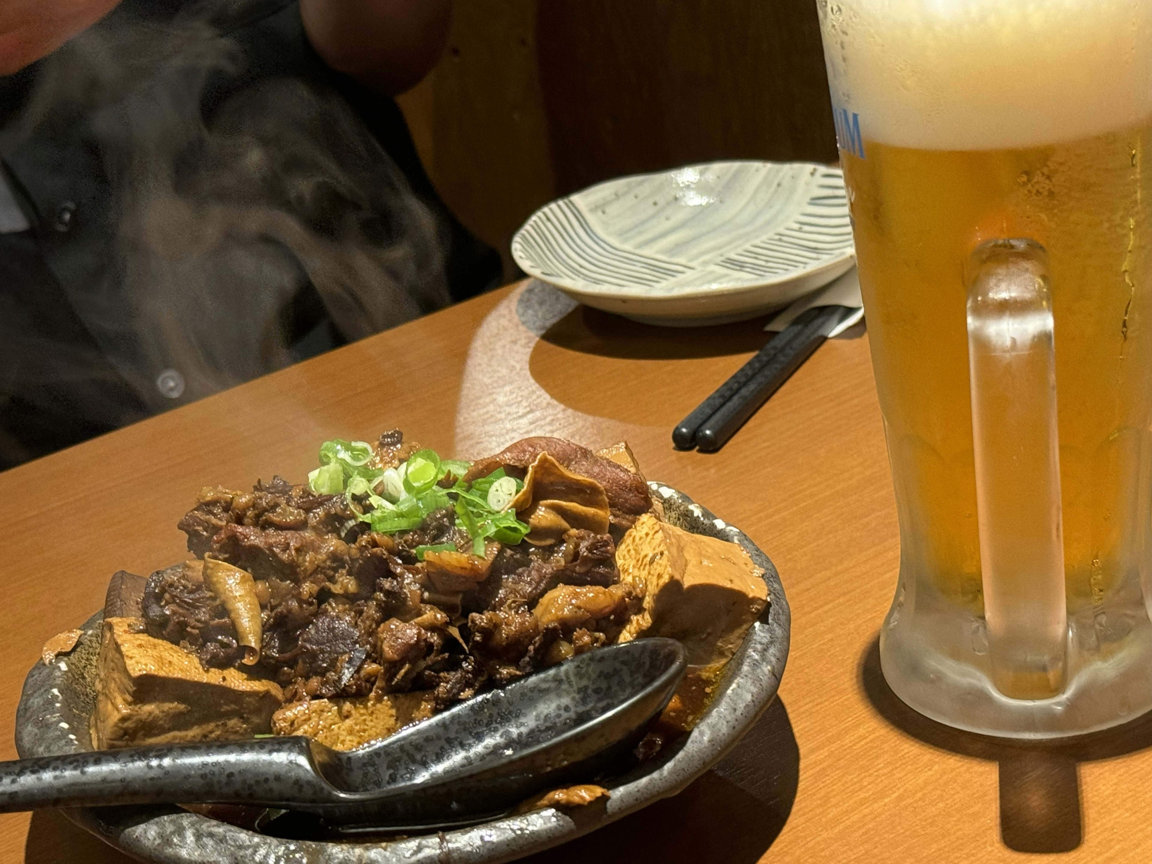 Steaming meat dish served with a glass of beer