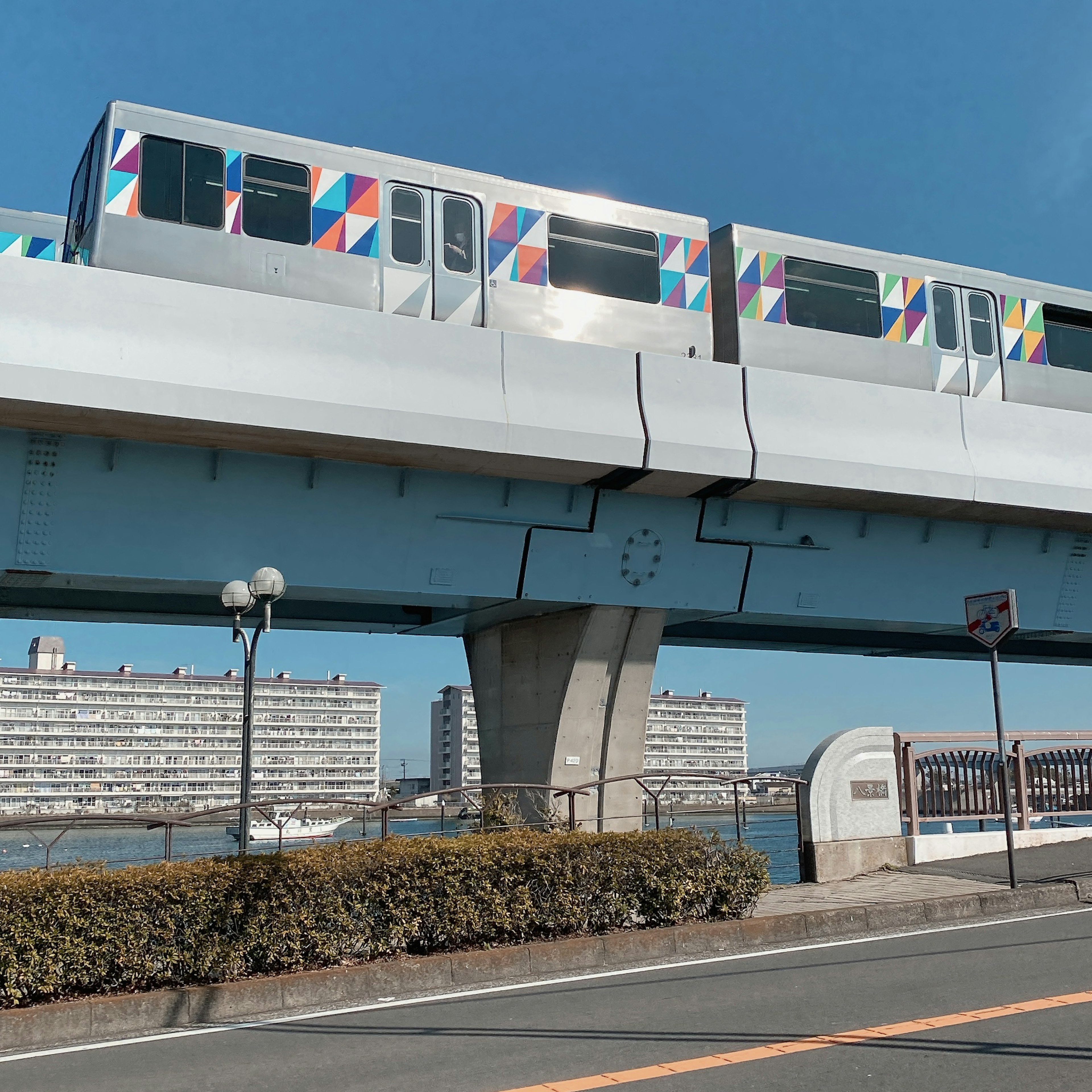 カラフルなデザインの高架電車が青空の下を走っている