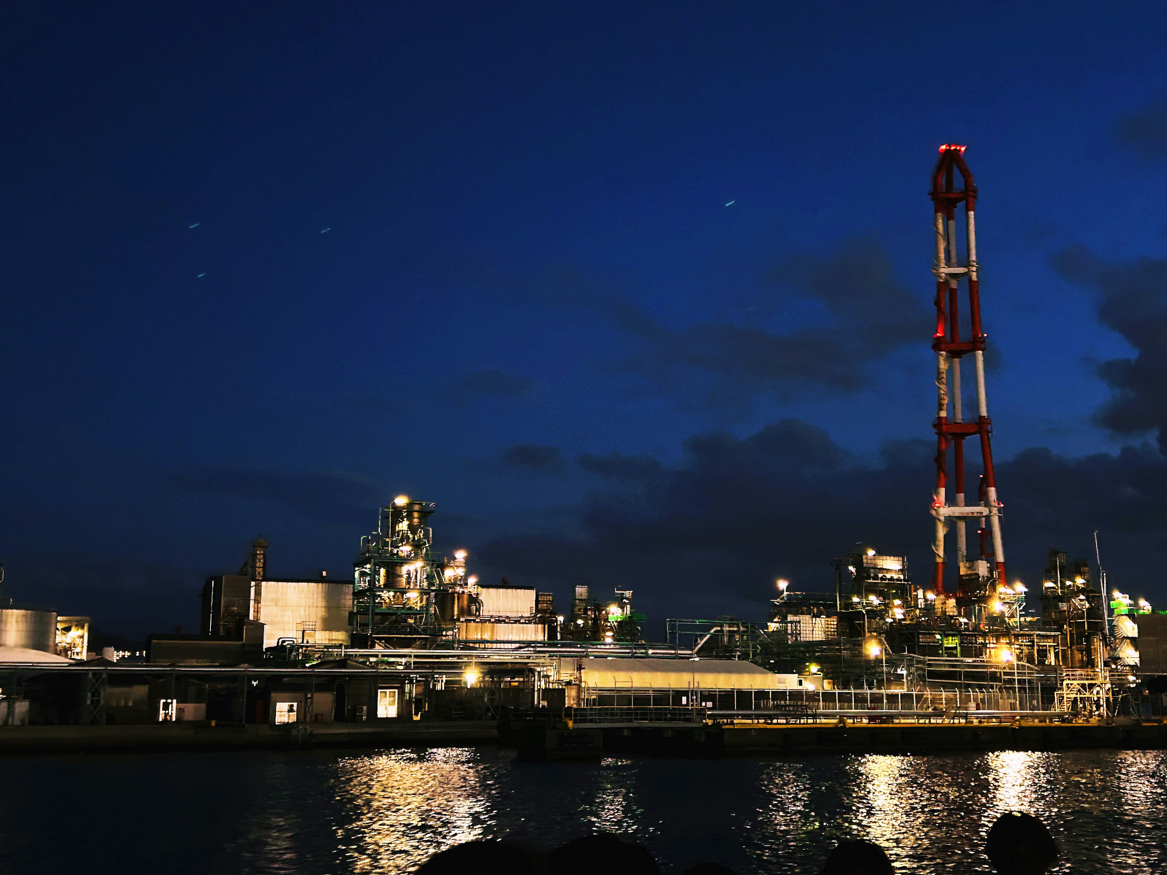 Installation industrielle illuminée la nuit avec reflet sur l'eau