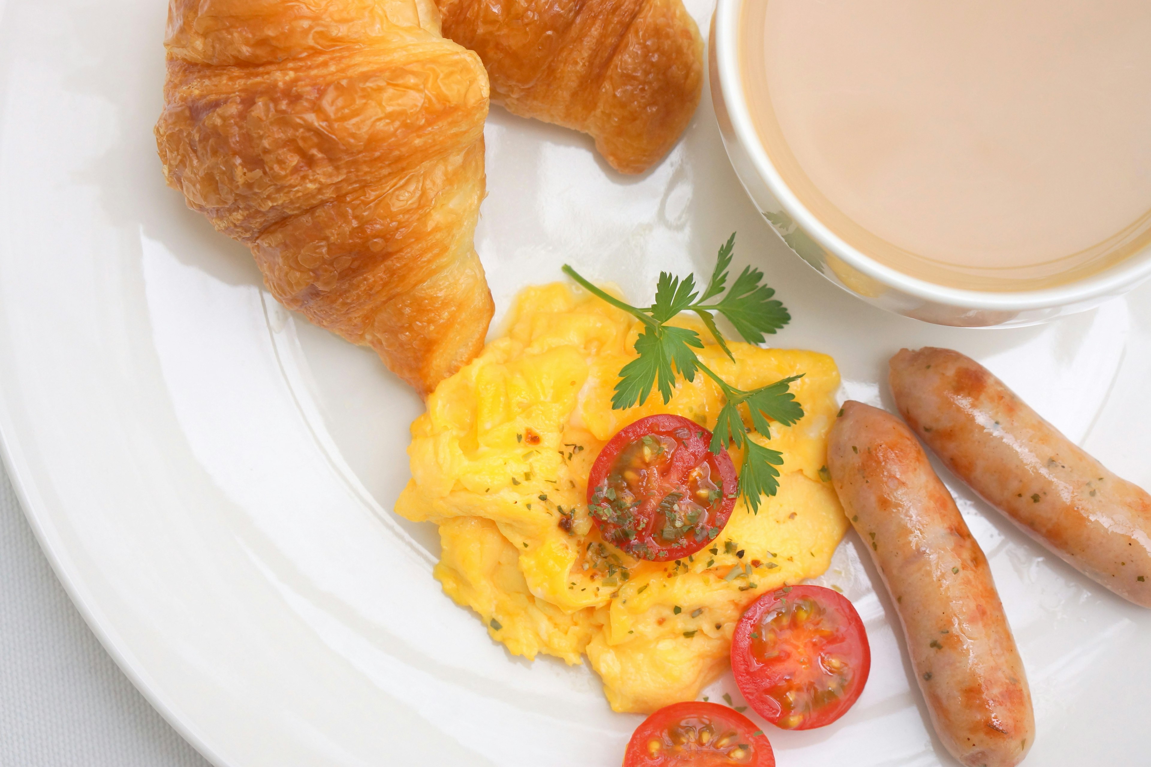 Frühstücksteller mit Croissants Rührei Kirschtomaten Würstchen und einer Tasse Kaffee