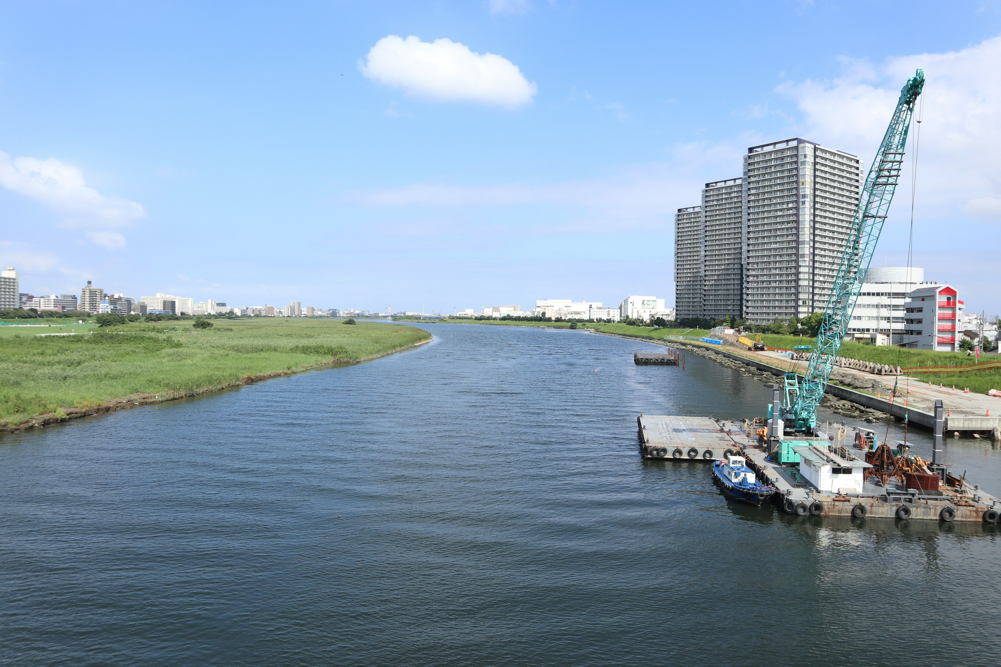 Scenic view of a river reflecting the blue sky with a large crane and modern buildings nearby