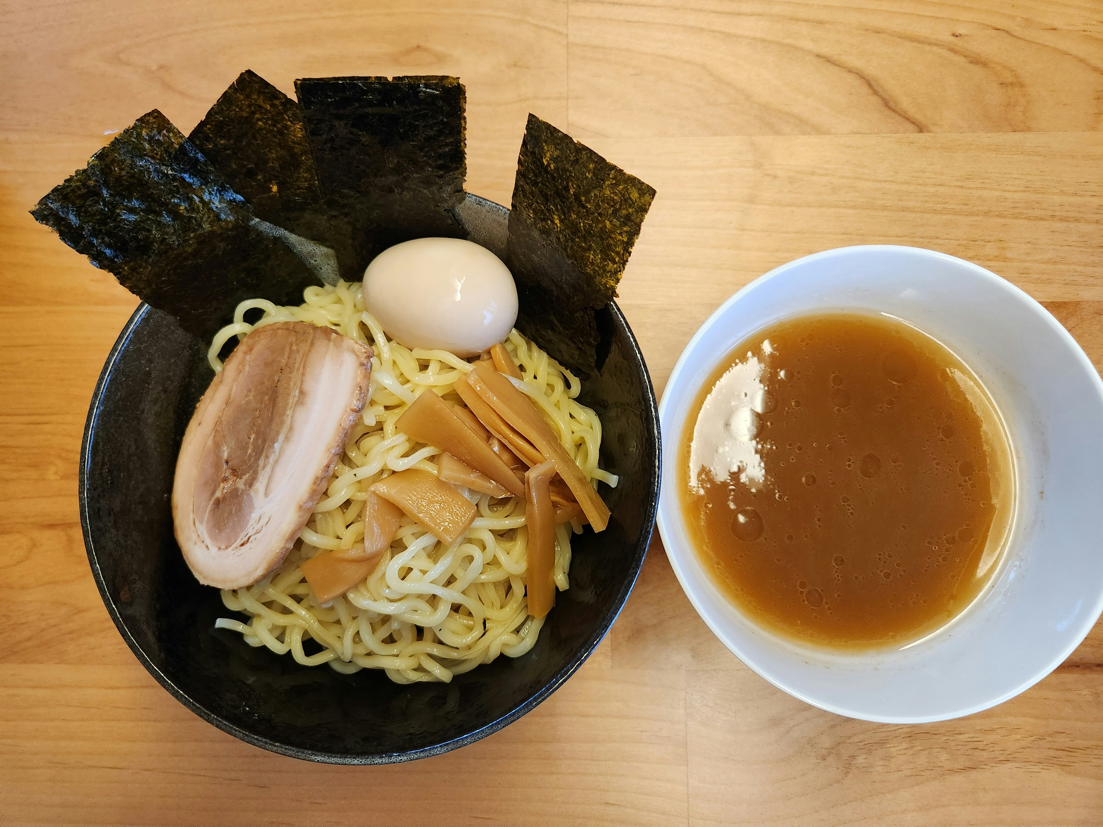 Immagine di ramen servito in una ciotola nera con salsa di immersione con noodles guarniti con chashu, germogli di bambù, uovo sodo e nori