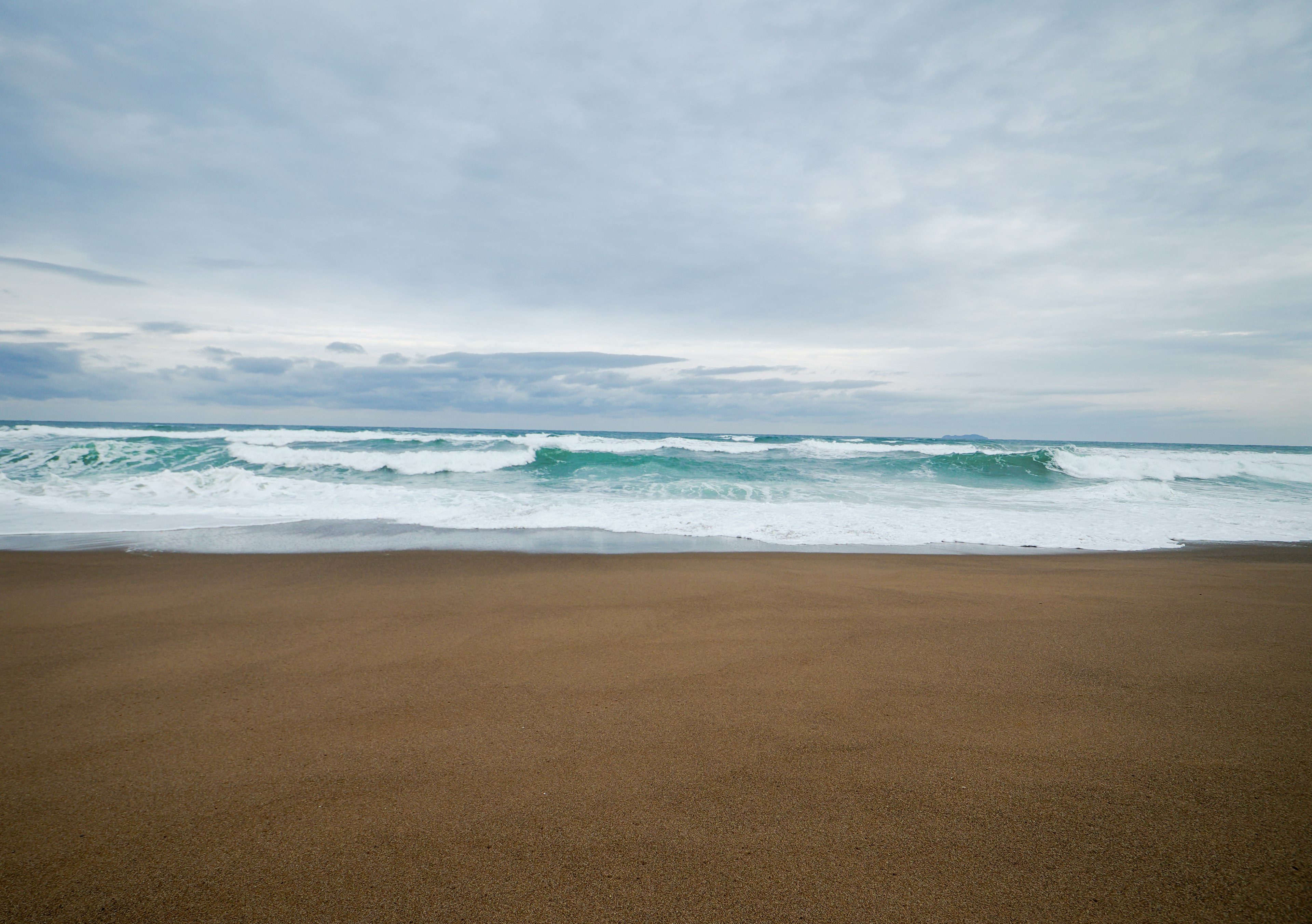 Vagues se brisant sur une plage de sable sous un ciel nuageux