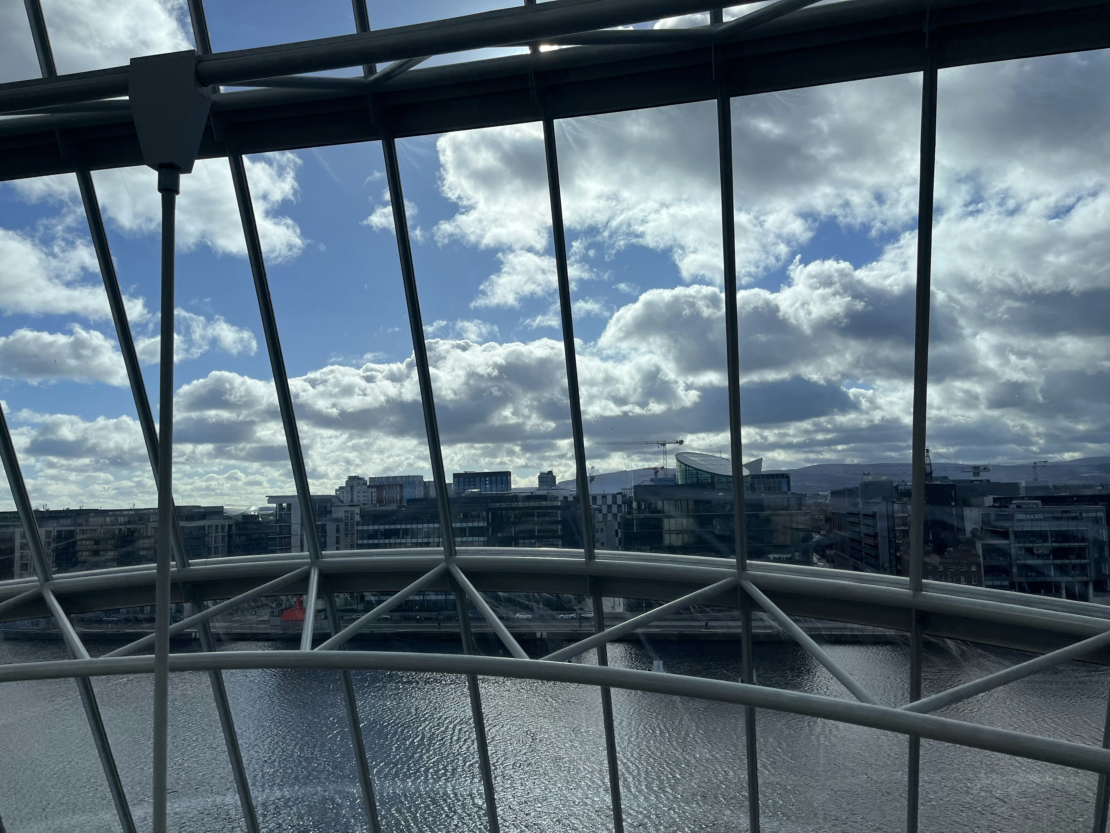 Cityscape view through a glass structure with clouds in the blue sky