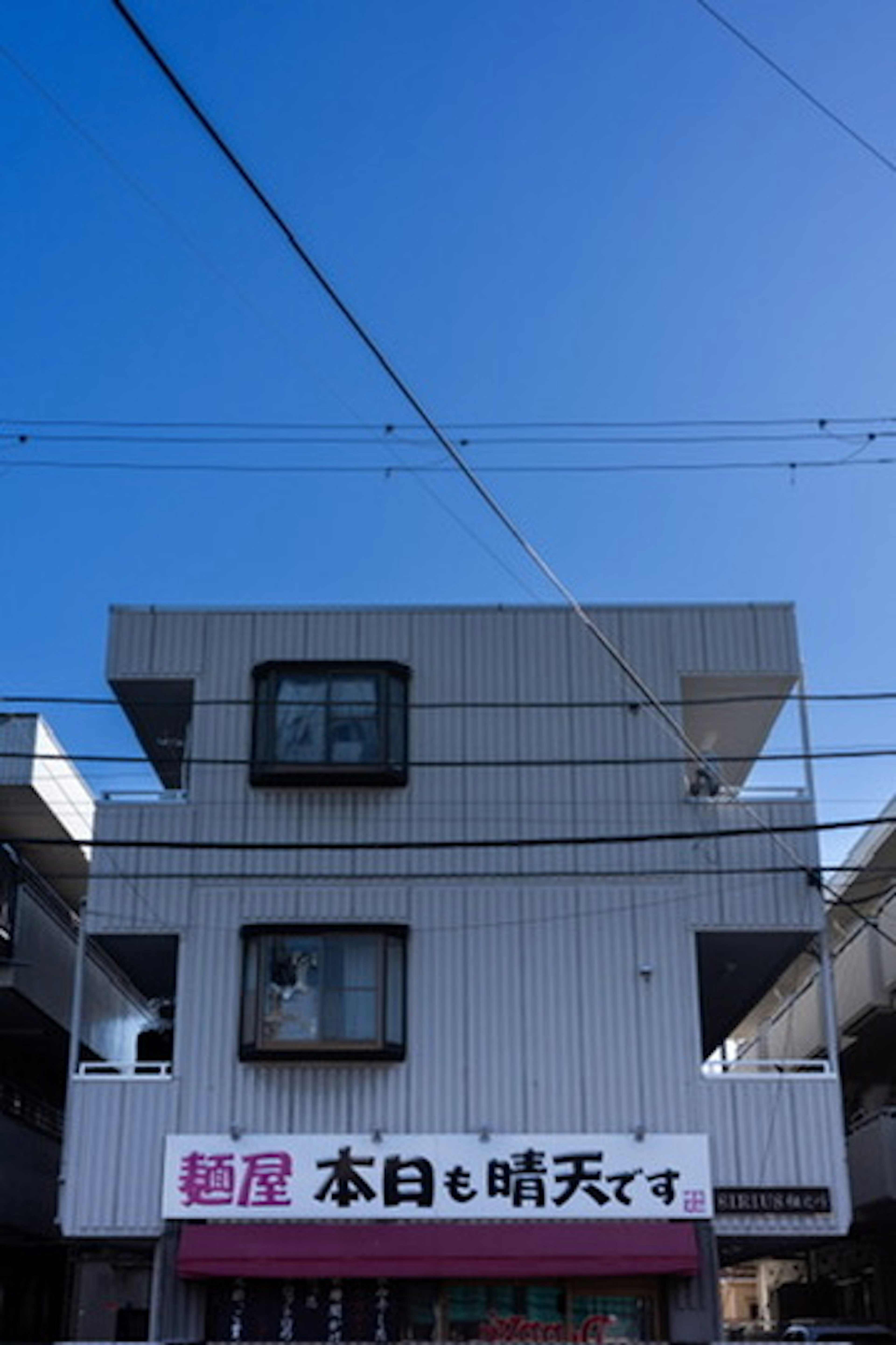 Edificio blanco bajo un cielo azul con un letrero