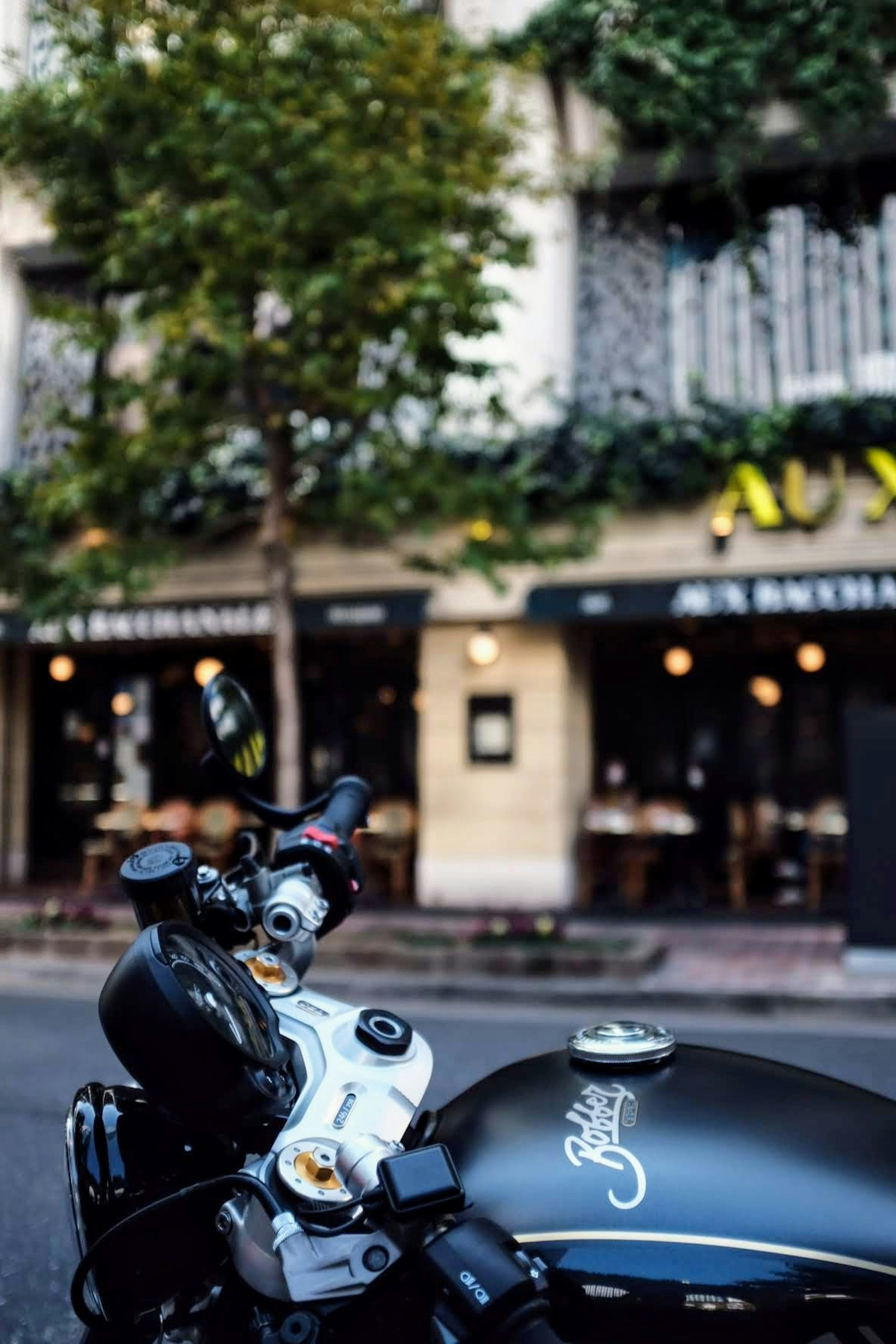 Close-up of a black motorcycle handlebar with a cafe in the background