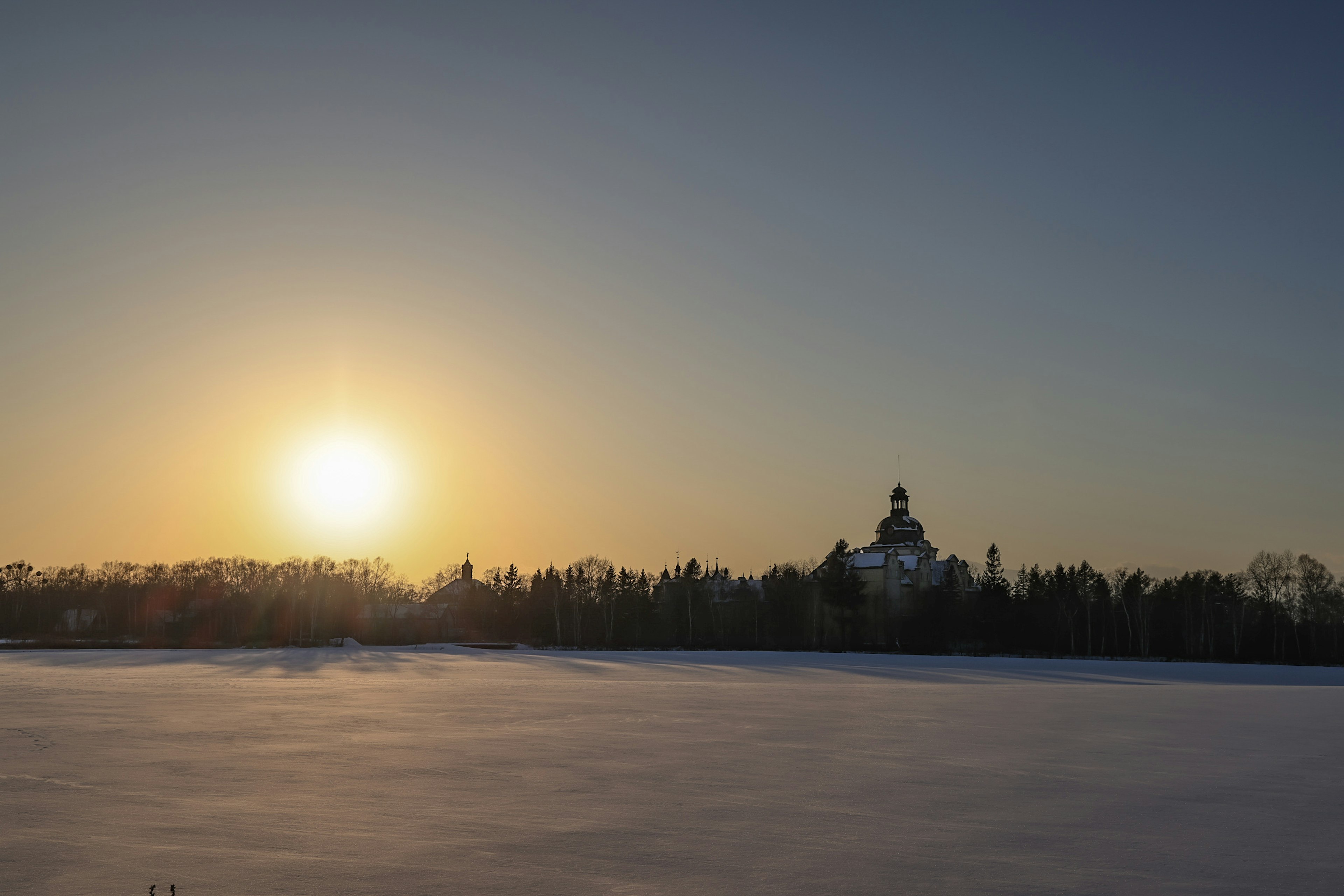 Setting sun over a snowy landscape and distant trees