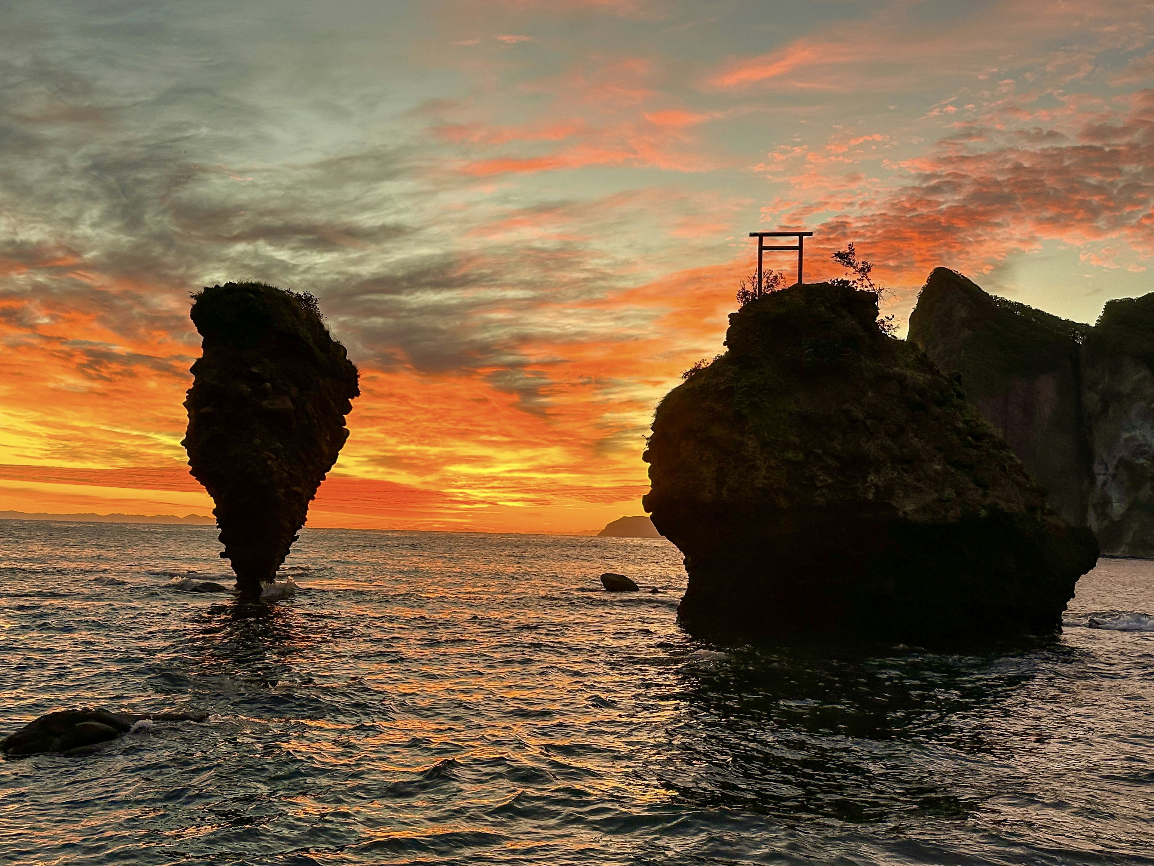 Dua batu besar berdiri di lautan saat matahari terbenam dengan torii