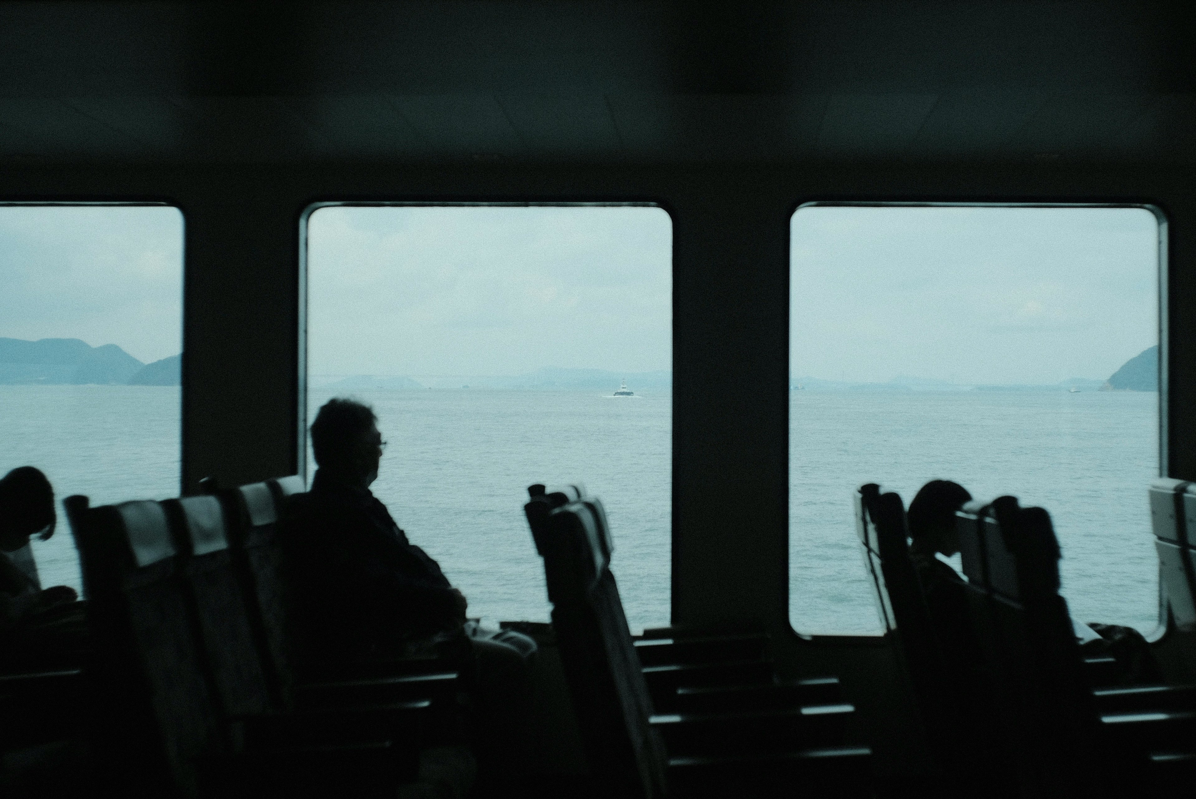 Intérieur d'un ferry avec des passagers en silhouette devant la mer