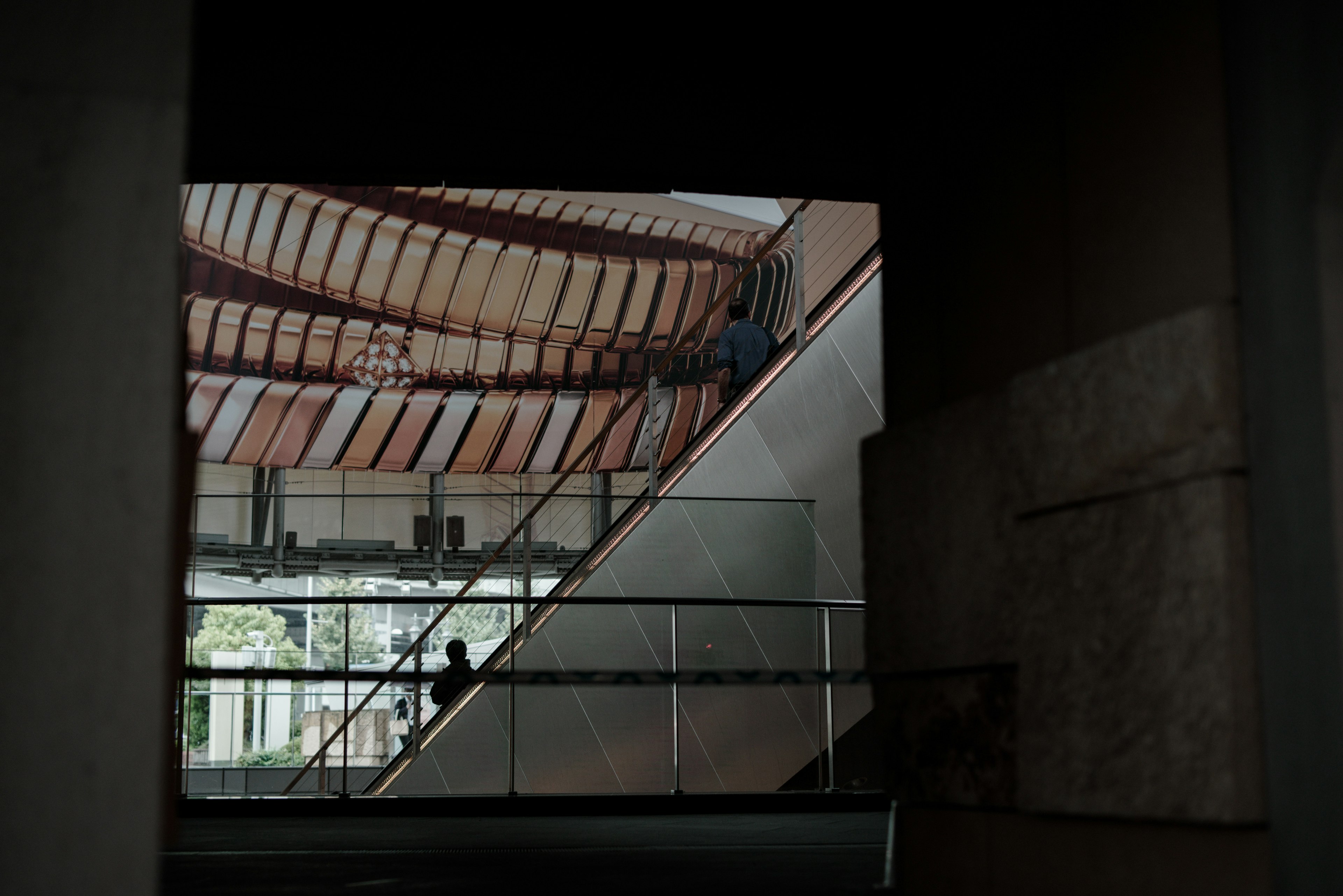 Interior de un edificio moderno con personas subiendo escaleras y un techo de madera