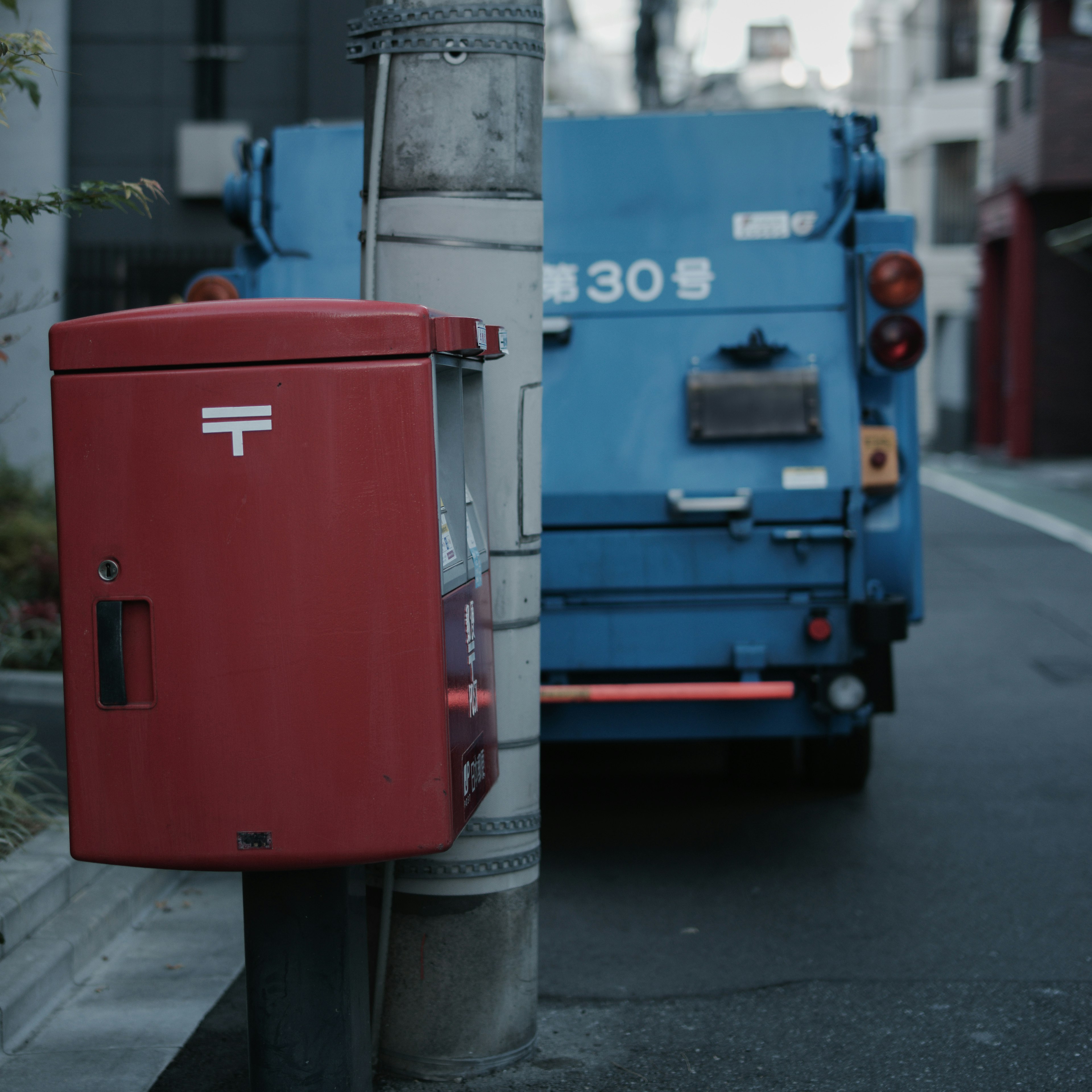 Boîte aux lettres rouge à côté d'un camion poubelle bleu au coin de la rue