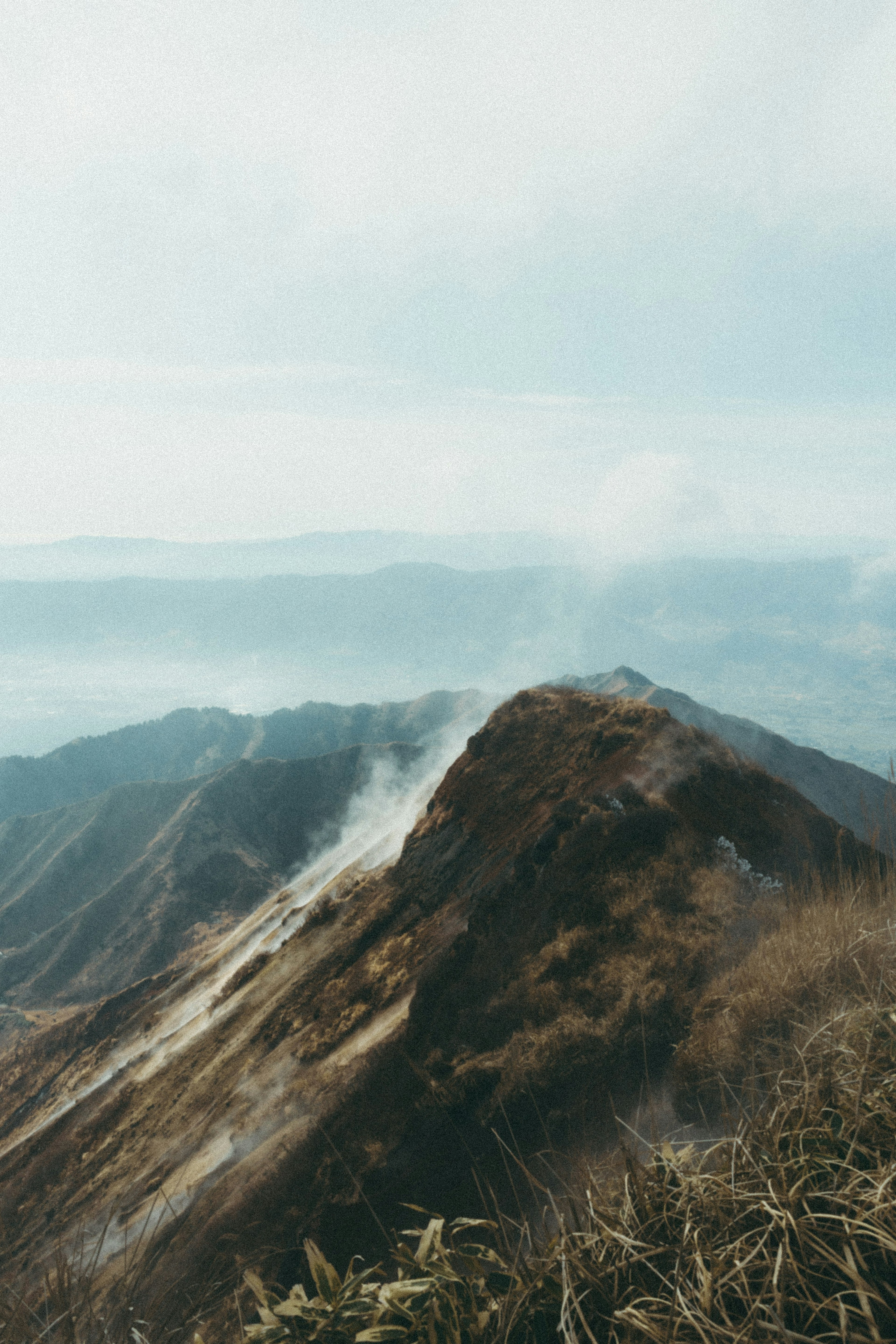 Paisaje montañoso brumoso con humo que sale de la cima hierba verde y suelo seco