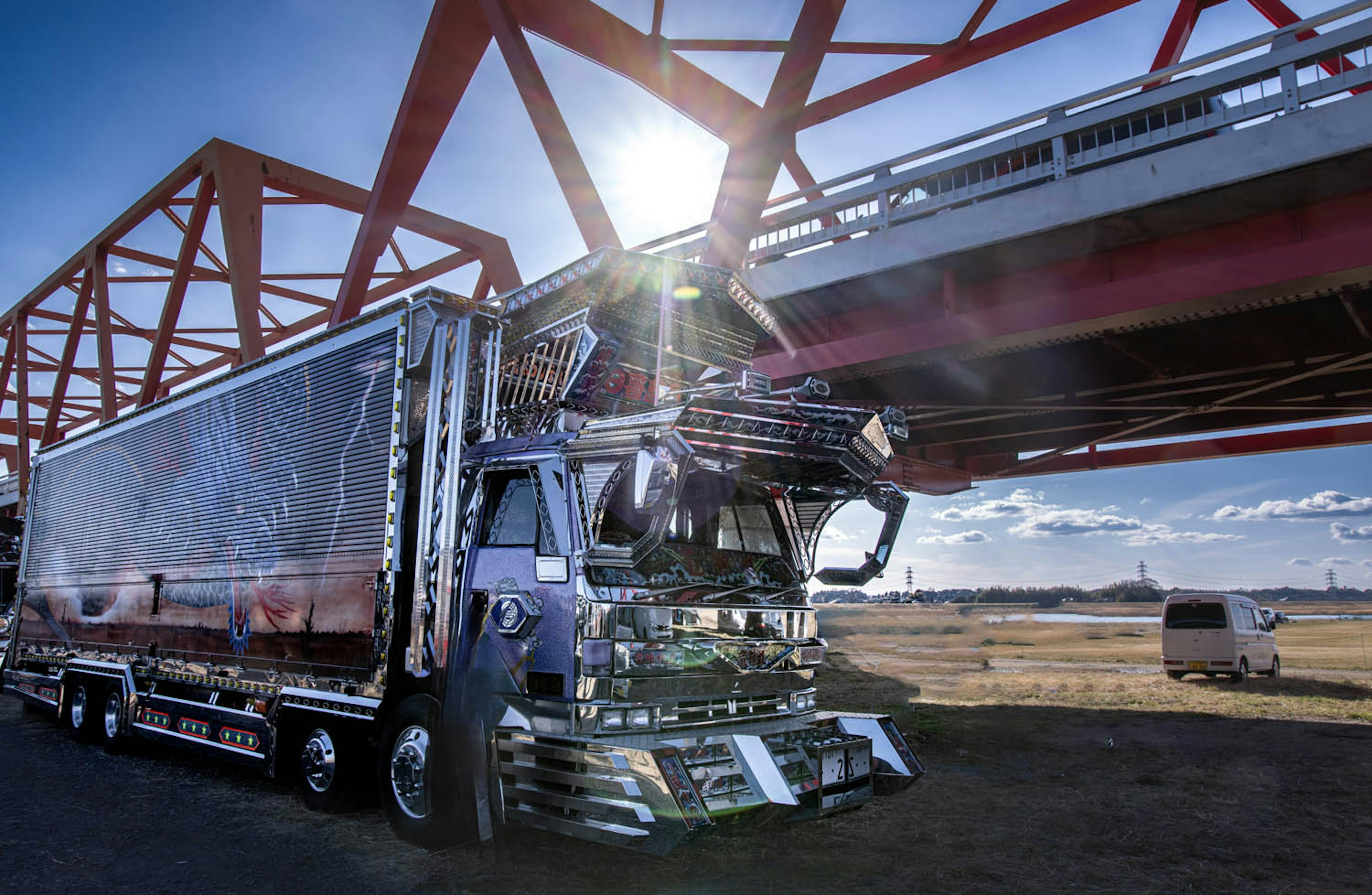 Ein glänzender Lkw, der unter einer roten Brücke parkt und Sonnenlicht reflektiert