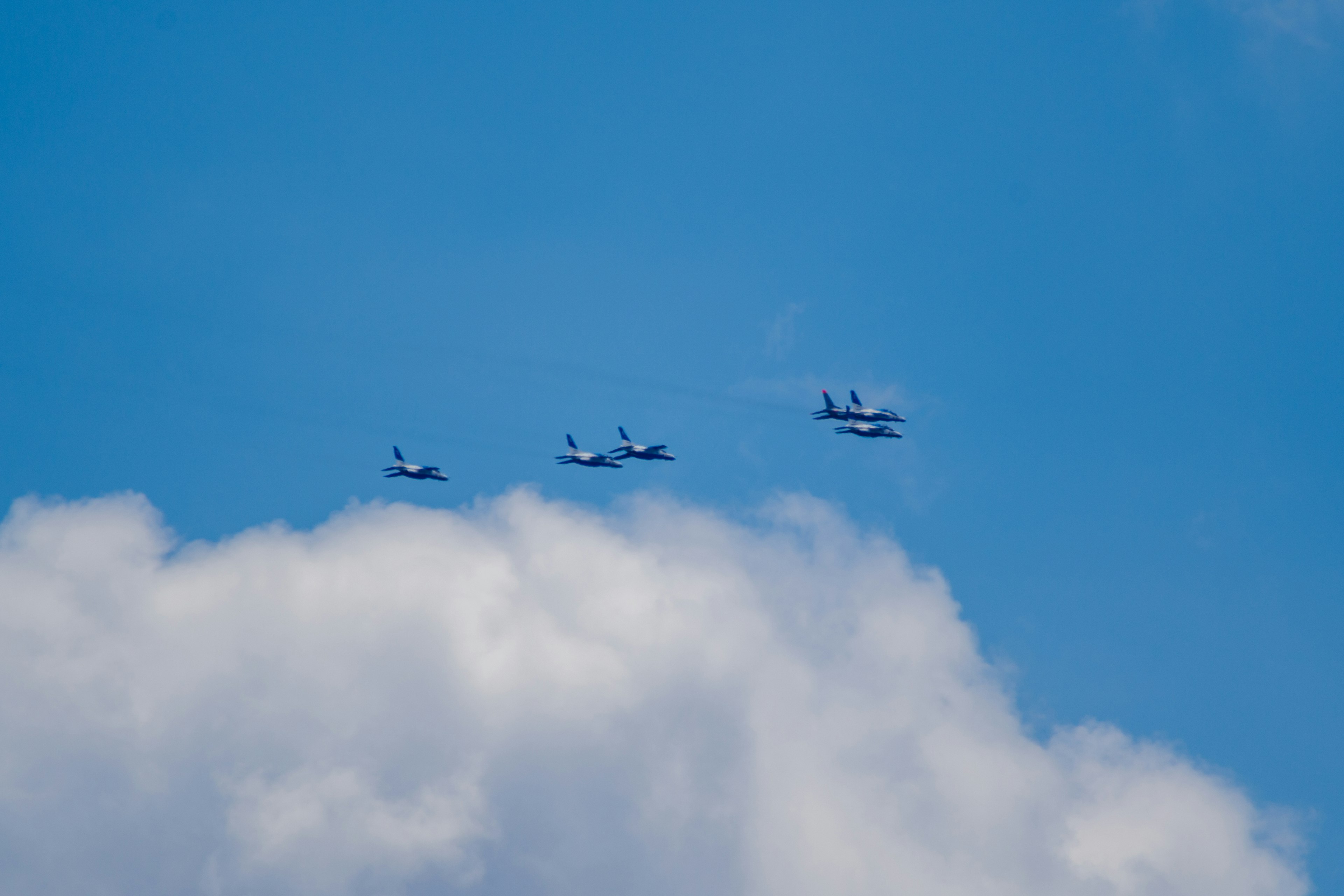 Four airplanes flying in a blue sky with white clouds