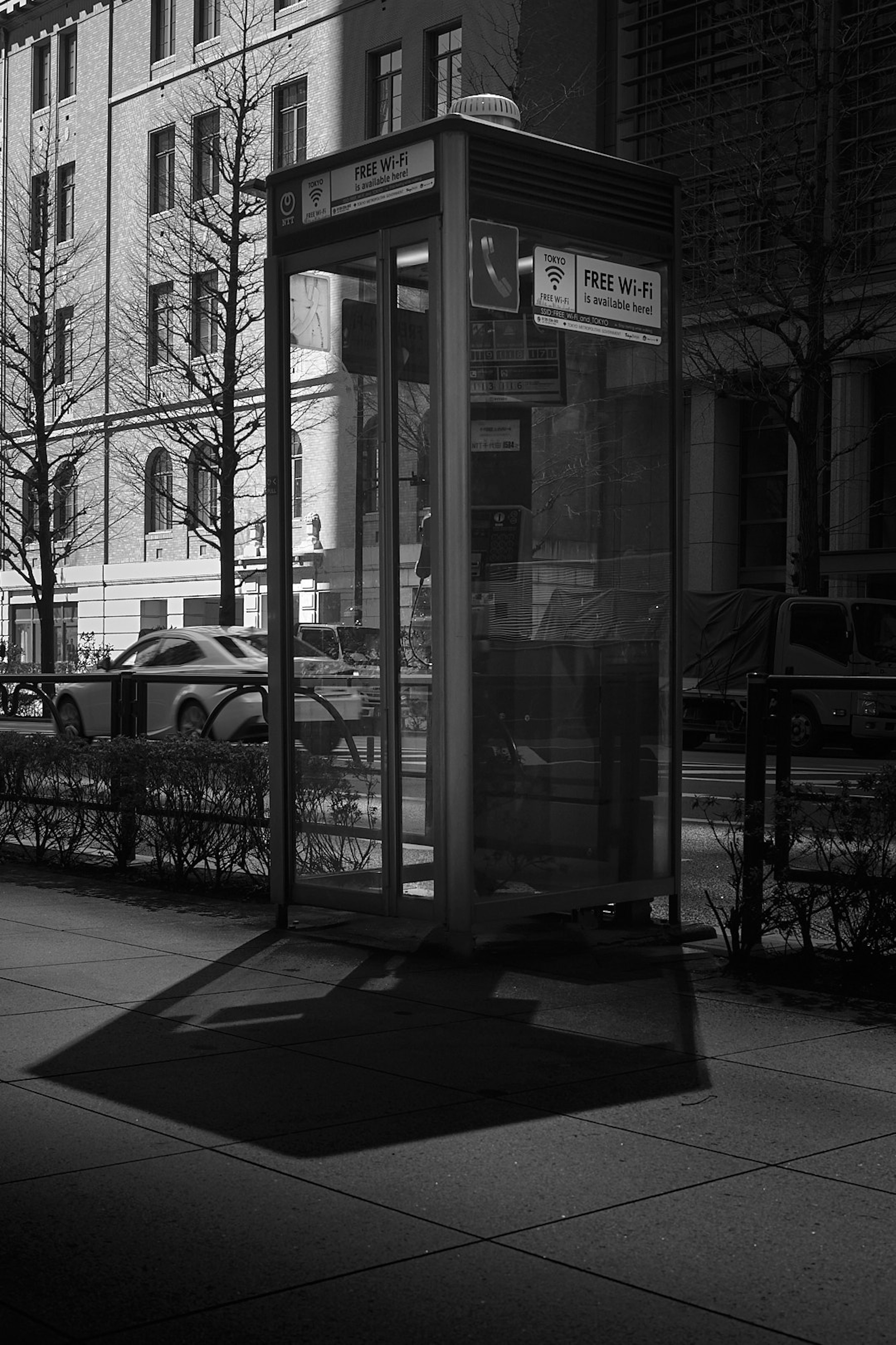 A phone booth casting a shadow on the sidewalk in a city setting