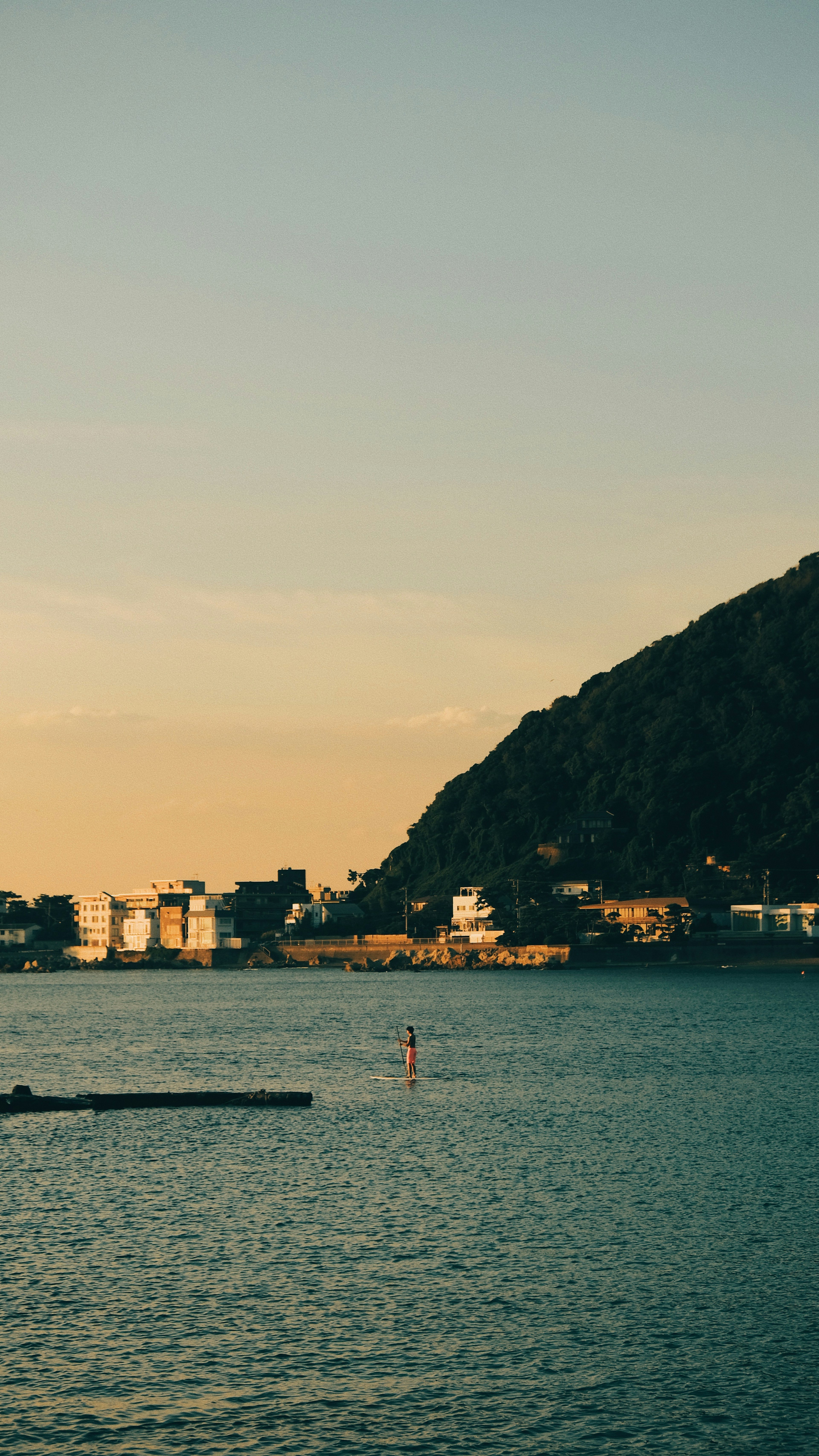 Un paddleboarder su acque calme con uno sfondo montano al tramonto