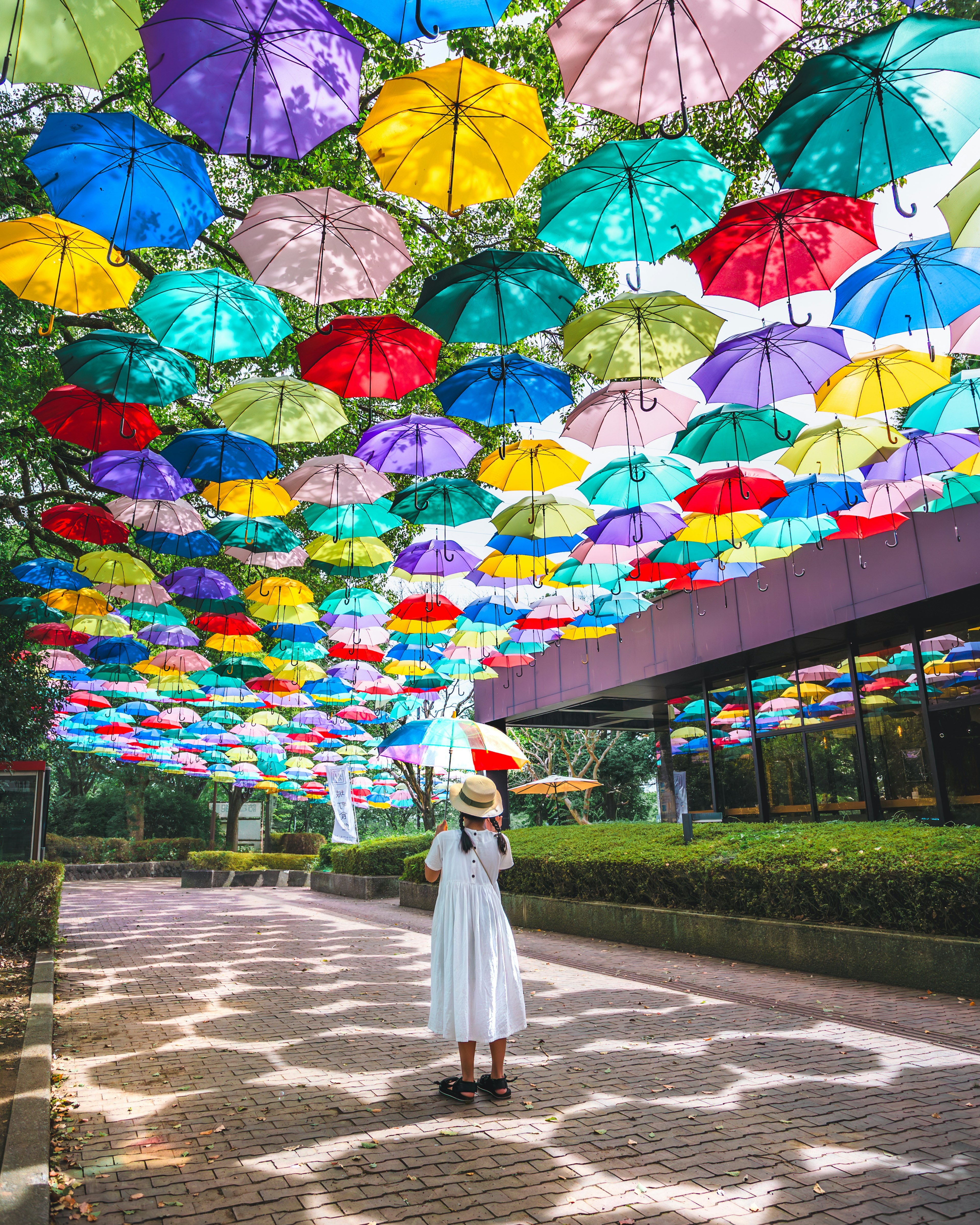 Une femme se tenant sous une installation colorée de parapluies