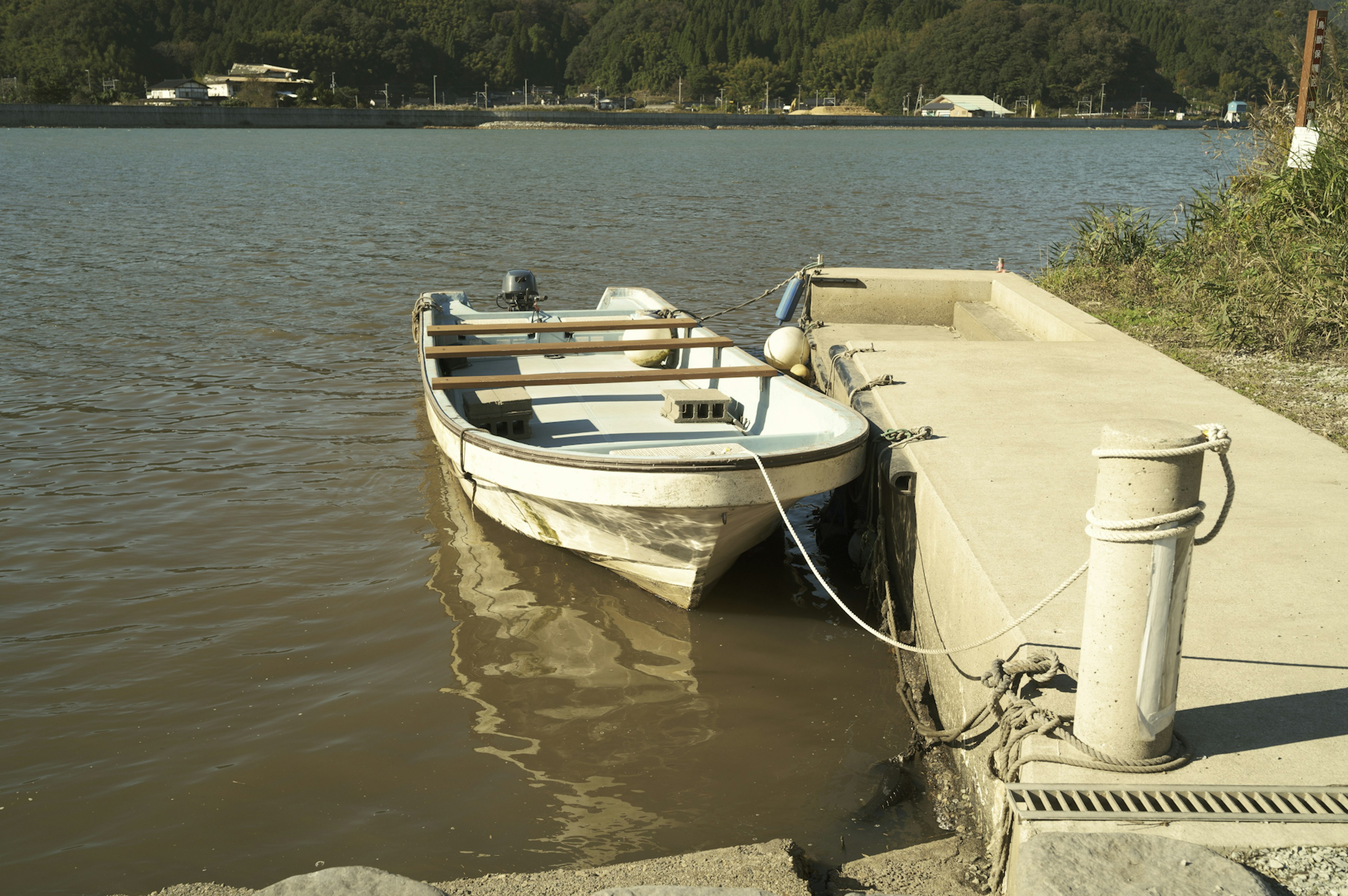 A small boat docked at a serene waterfront with a concrete pier