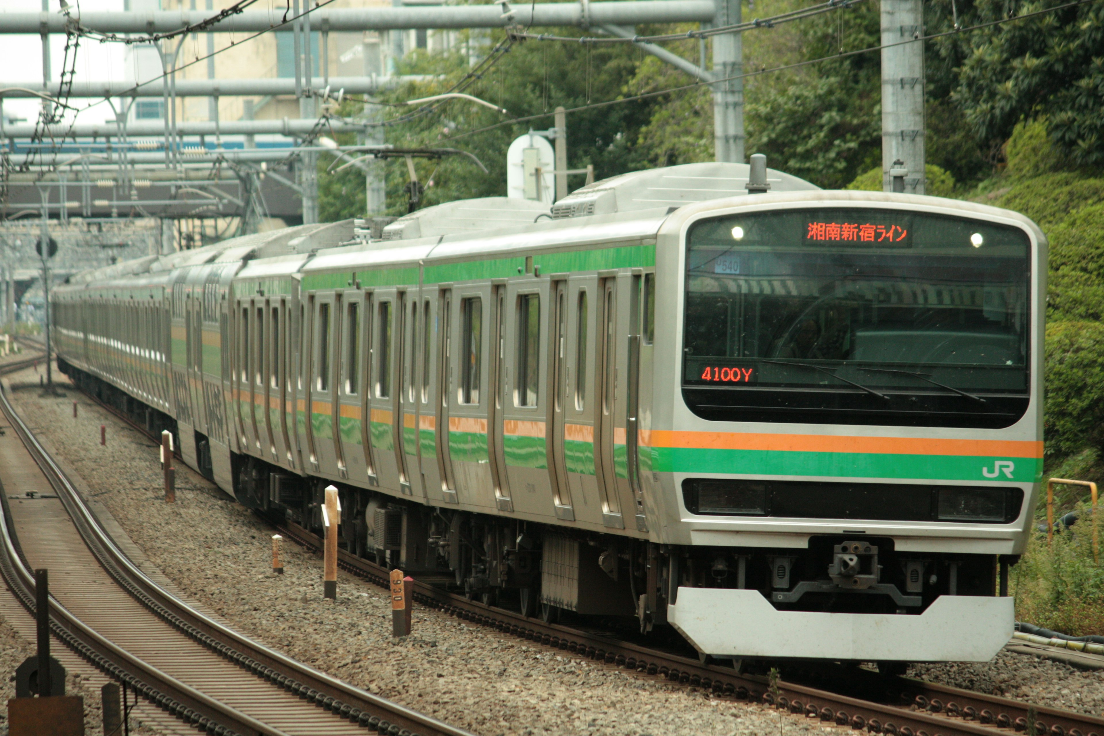 Sebuah kereta dengan garis hijau dan oranye berjalan di rel