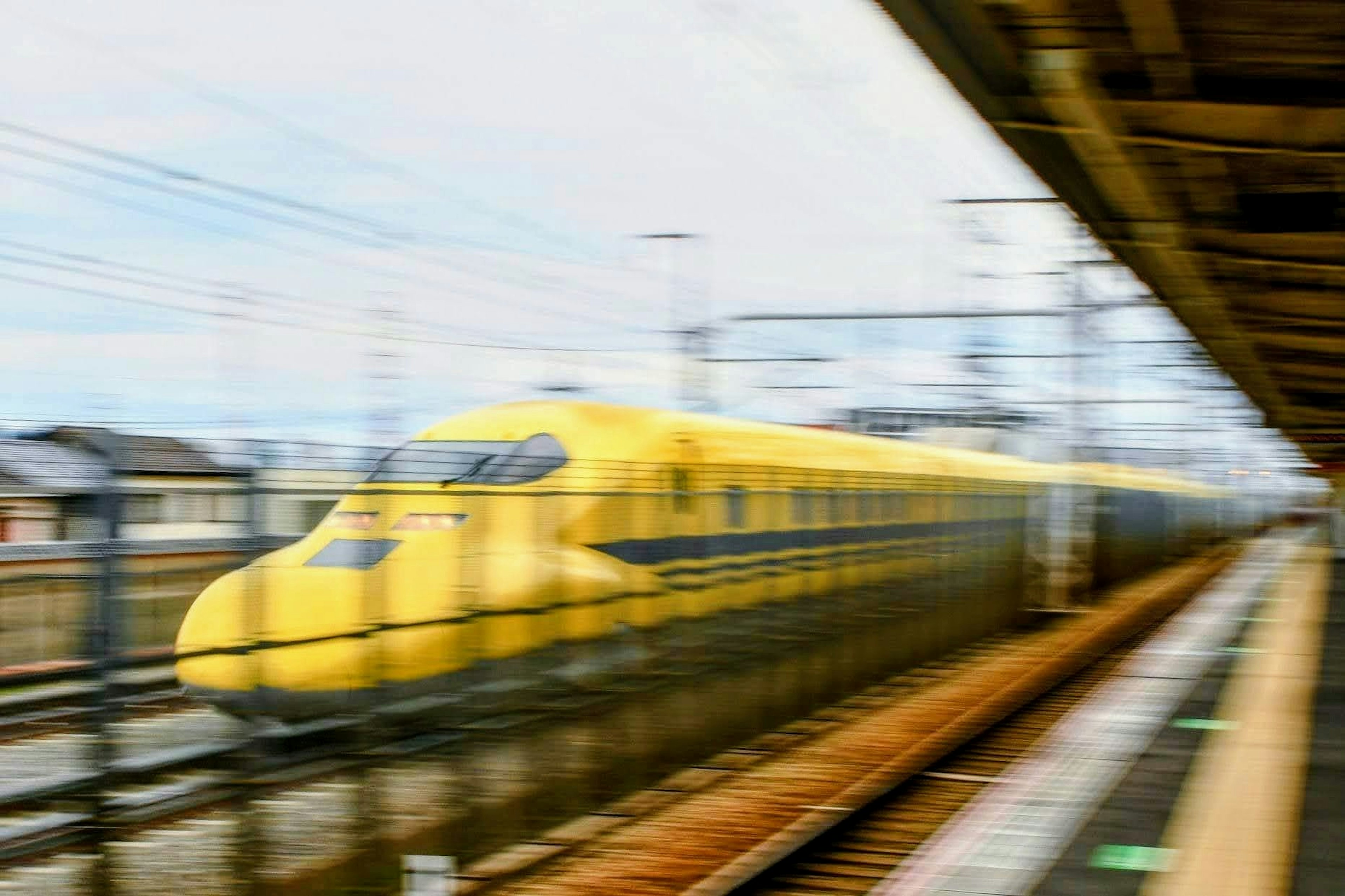 A yellow Shinkansen train passing through a station