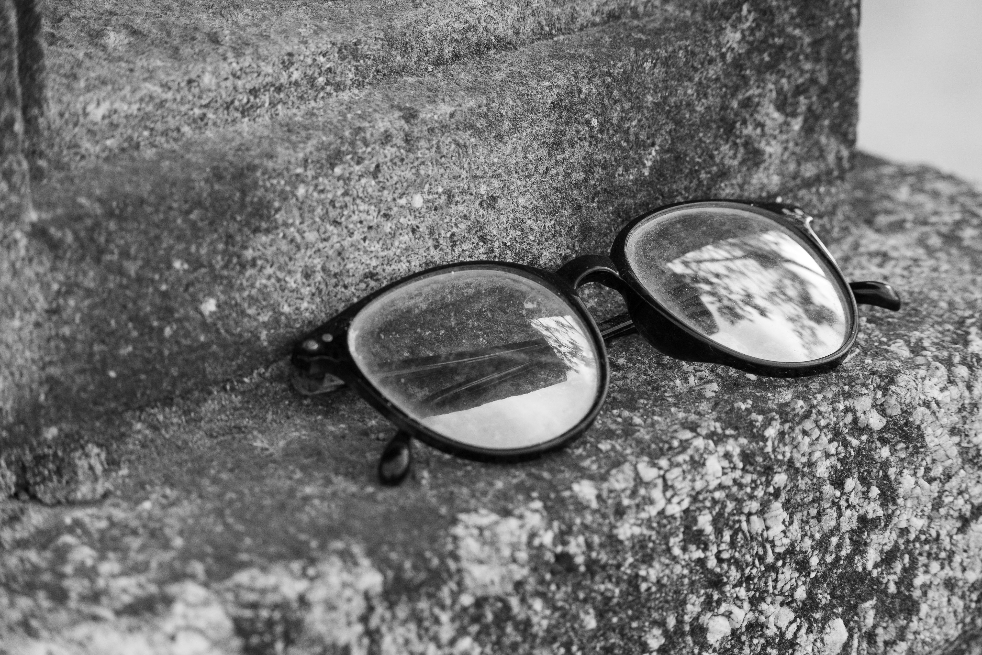 Black sunglasses resting on a stone surface in monochrome