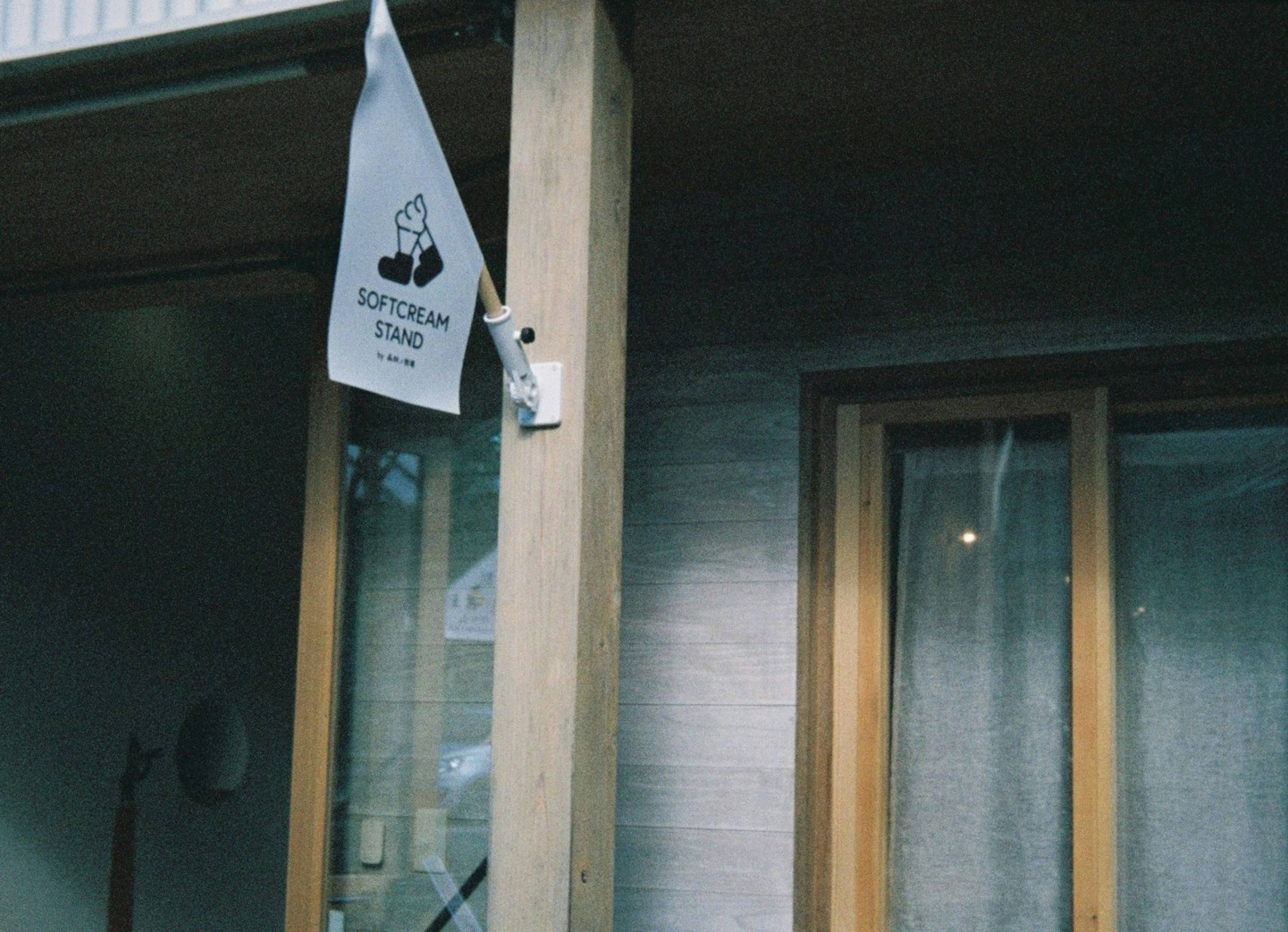 Exterior de un edificio con una bandera blanca colgada de un poste de madera y una ventana con marcos de madera y cortinas