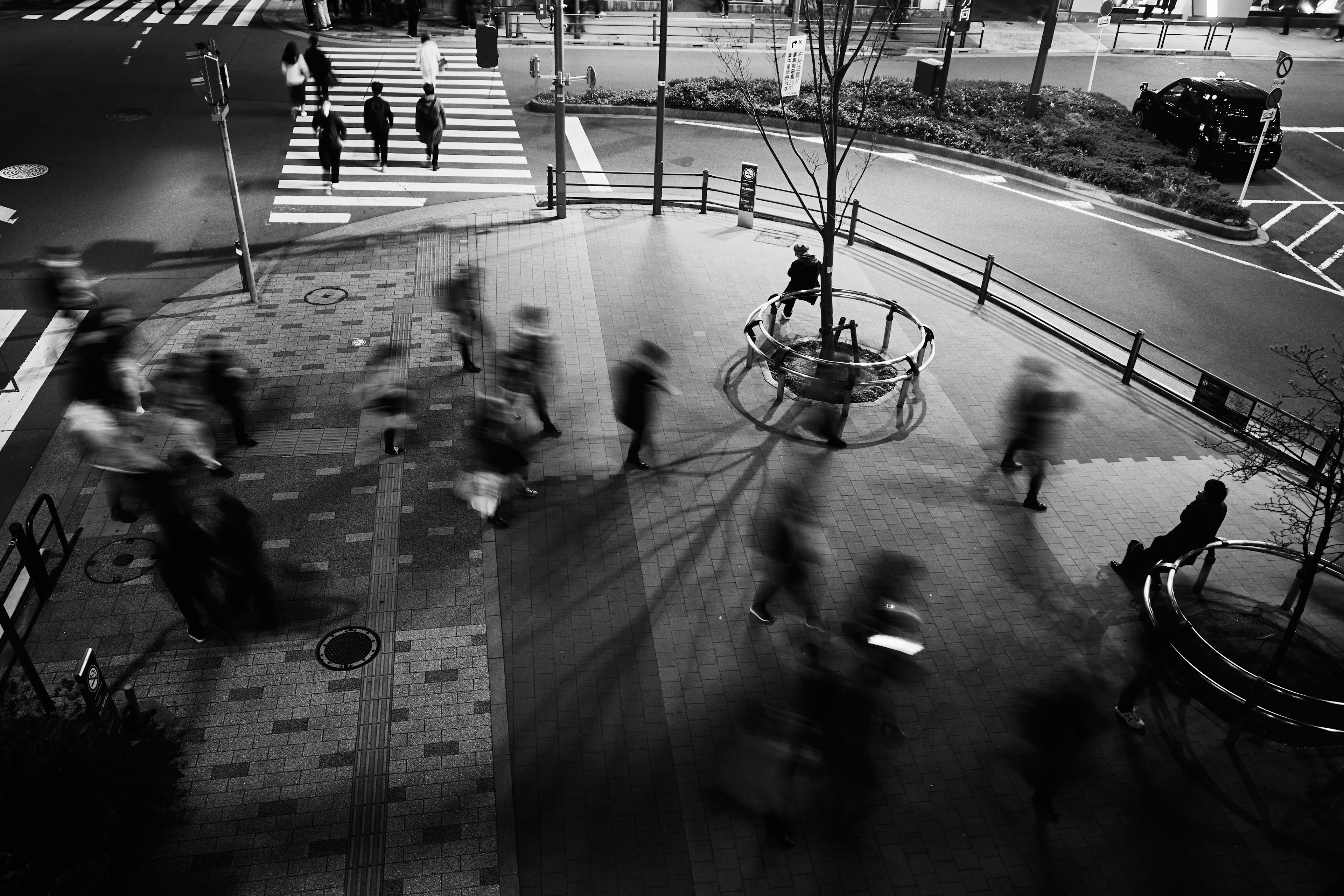 Schwarzweißfoto, das die Bewegung von Menschen an einer Straßenecke in der Nacht zeigt