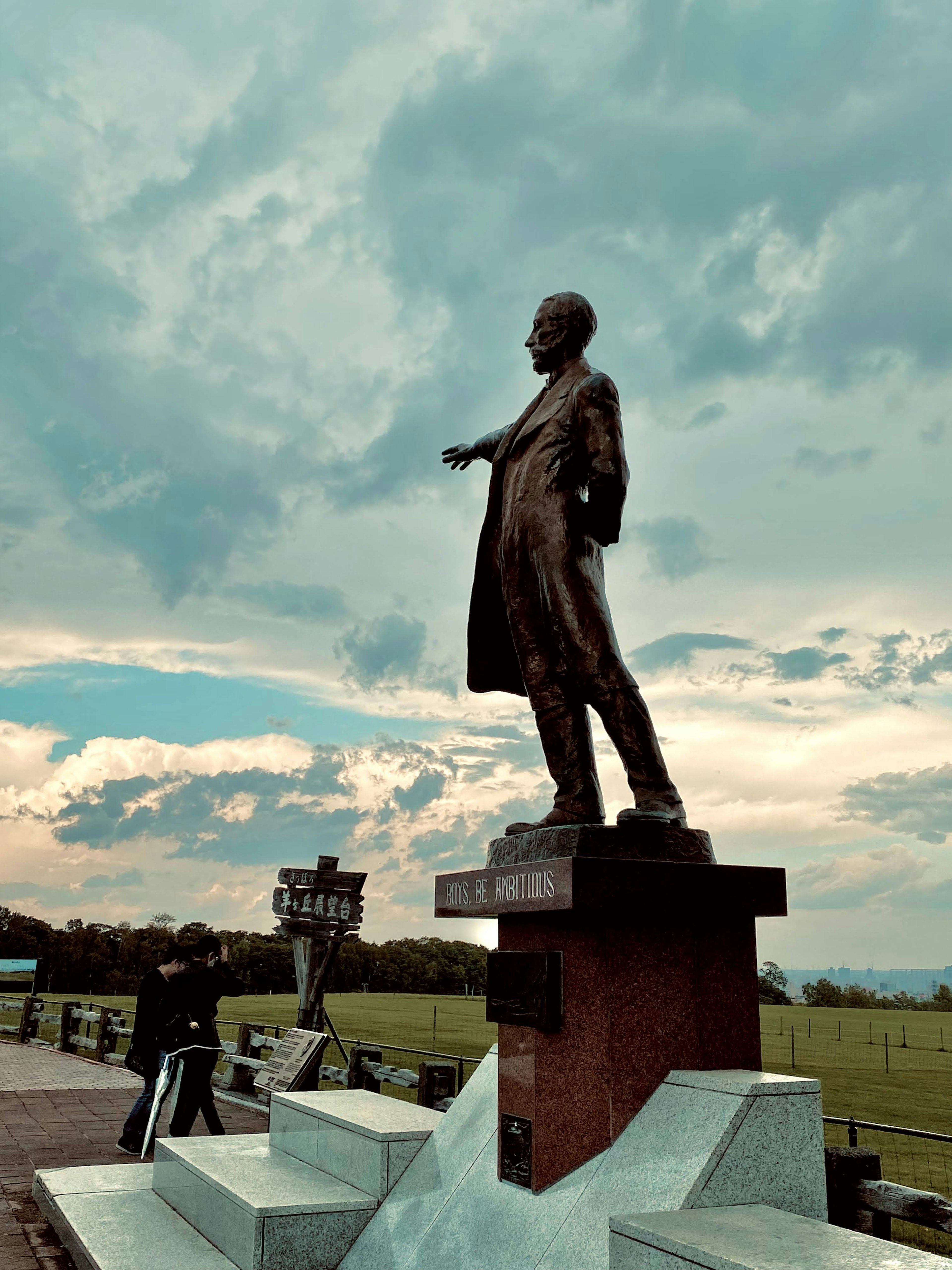 Bronze statue of a man standing in a park with a blue sky and clouds