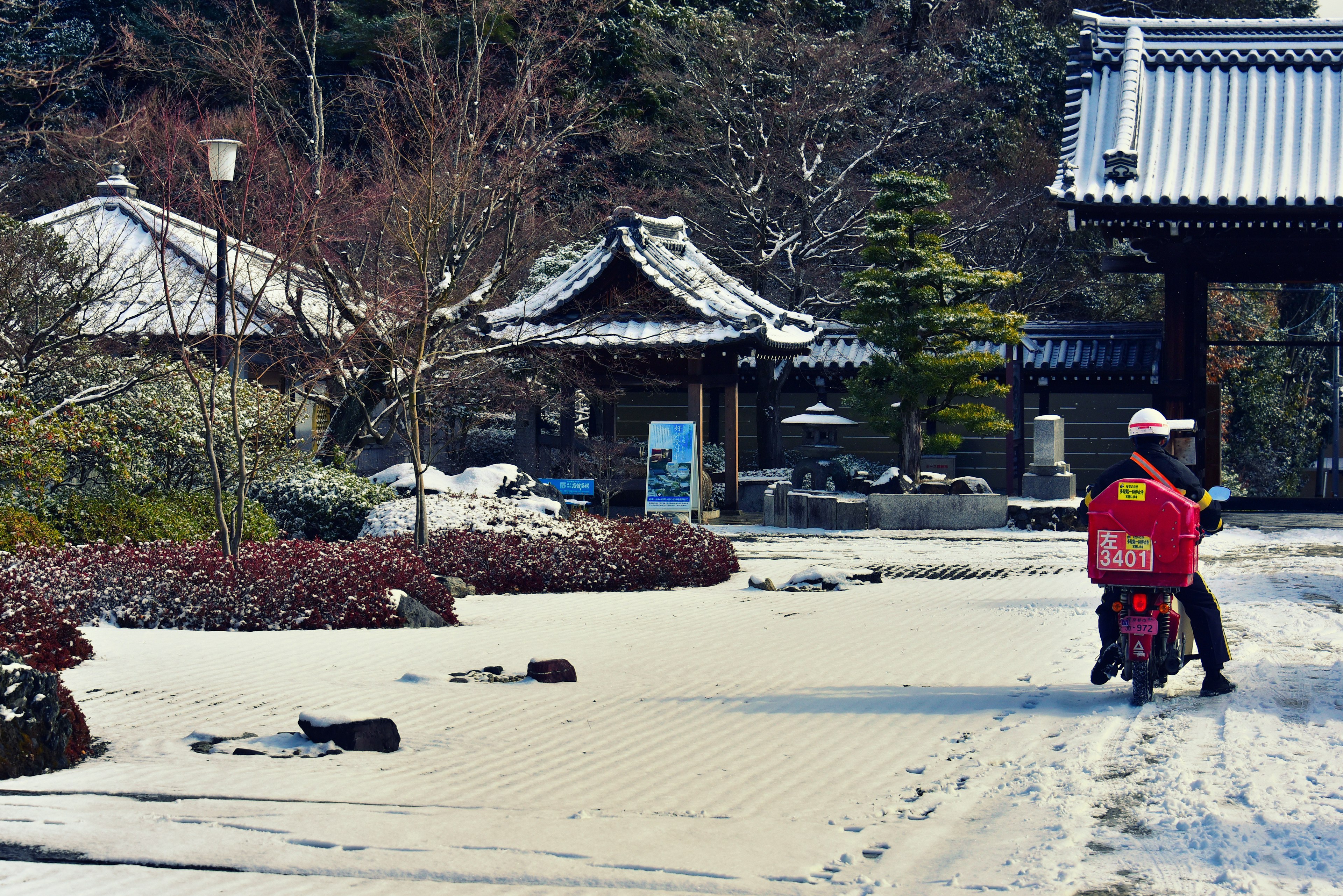 Delivery person riding a scooter in a snowy park with traditional buildings in the background