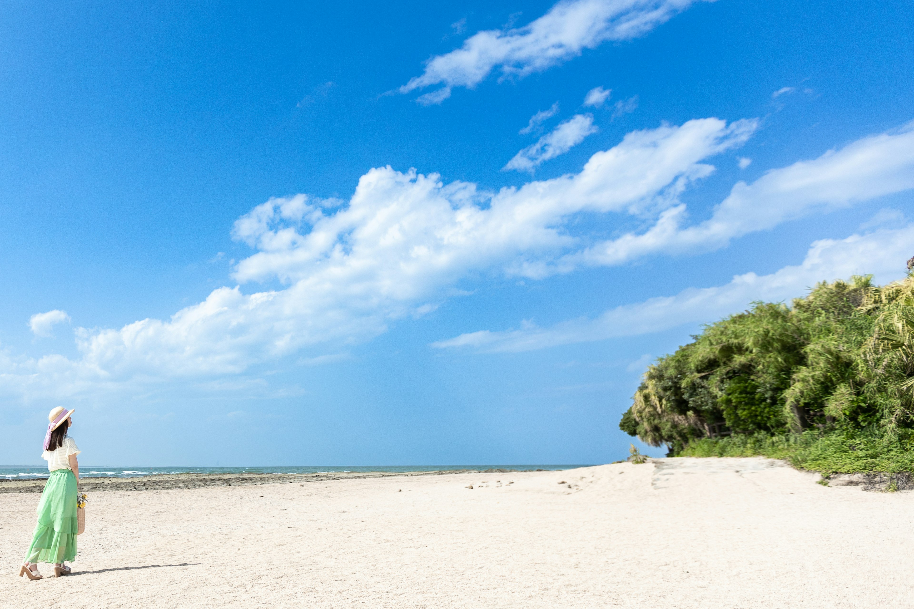 Una mujer con un vestido verde está de pie en una playa de arena blanca bajo un cielo azul