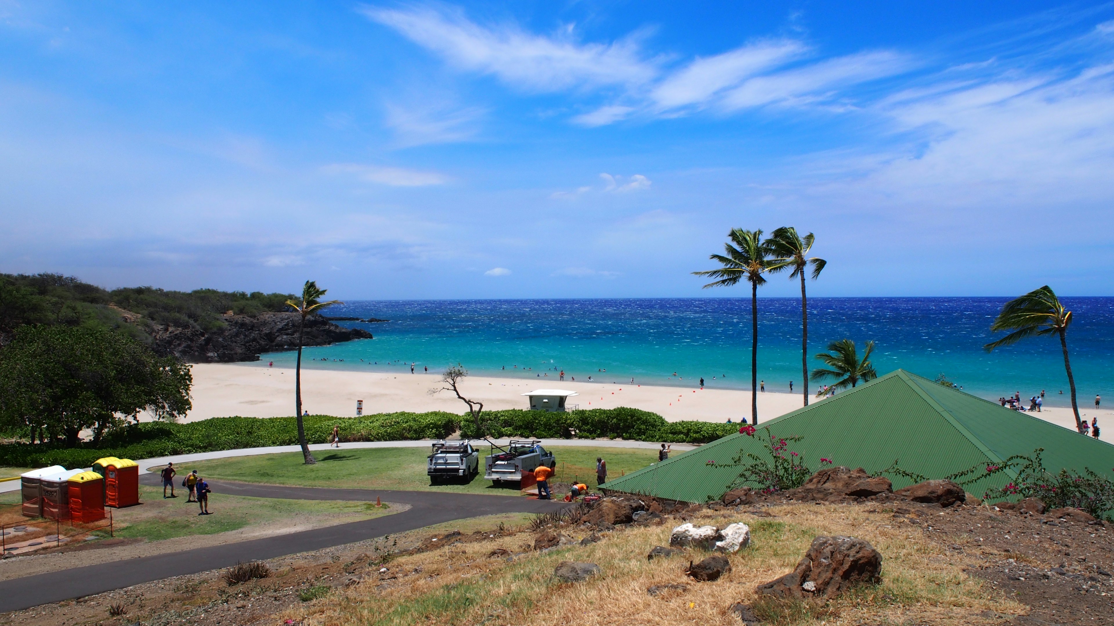 Vista de playa con océano azul y arena blanca colina verde y palmeras