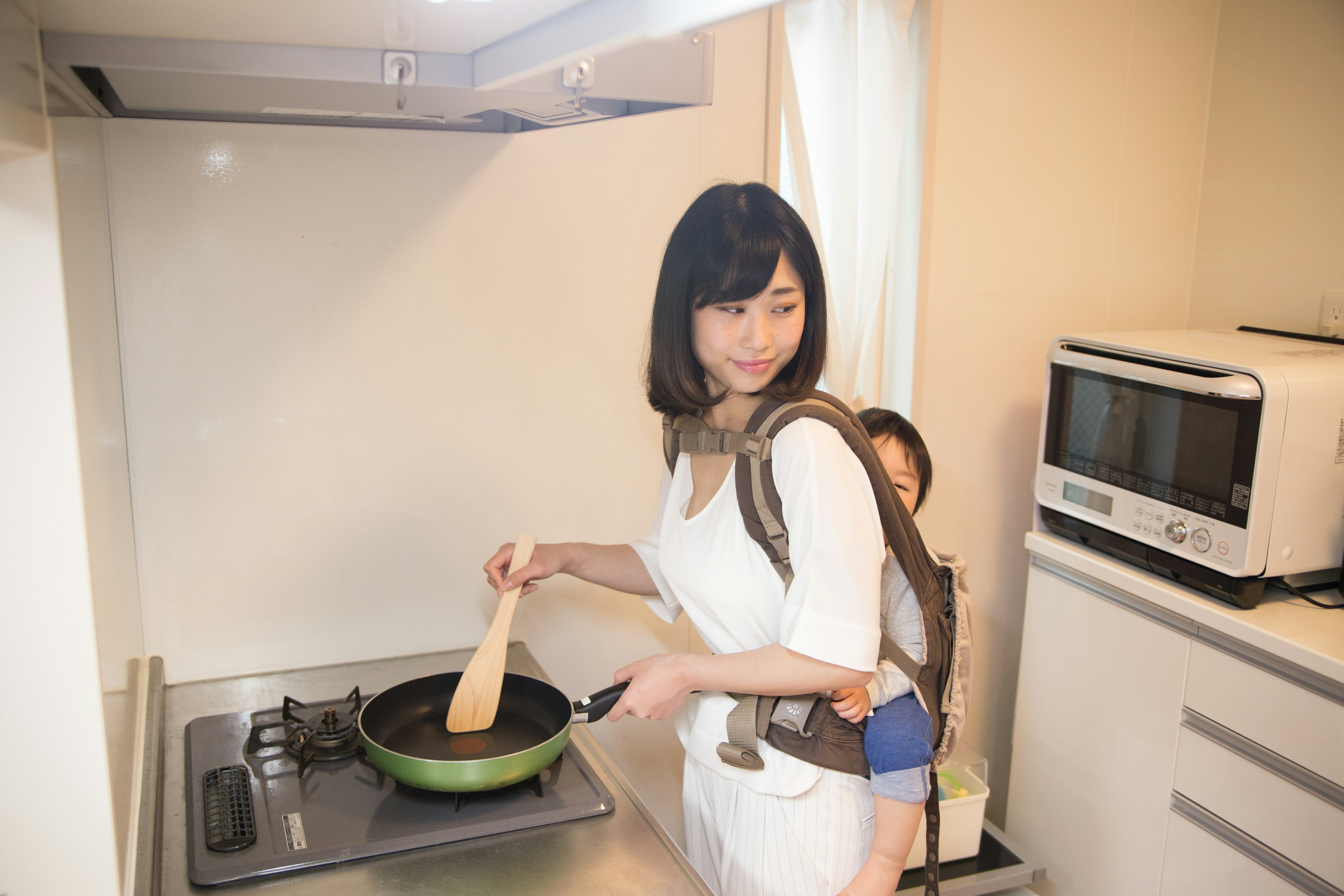 Mujer cocinando en una cocina con un niño en la espalda