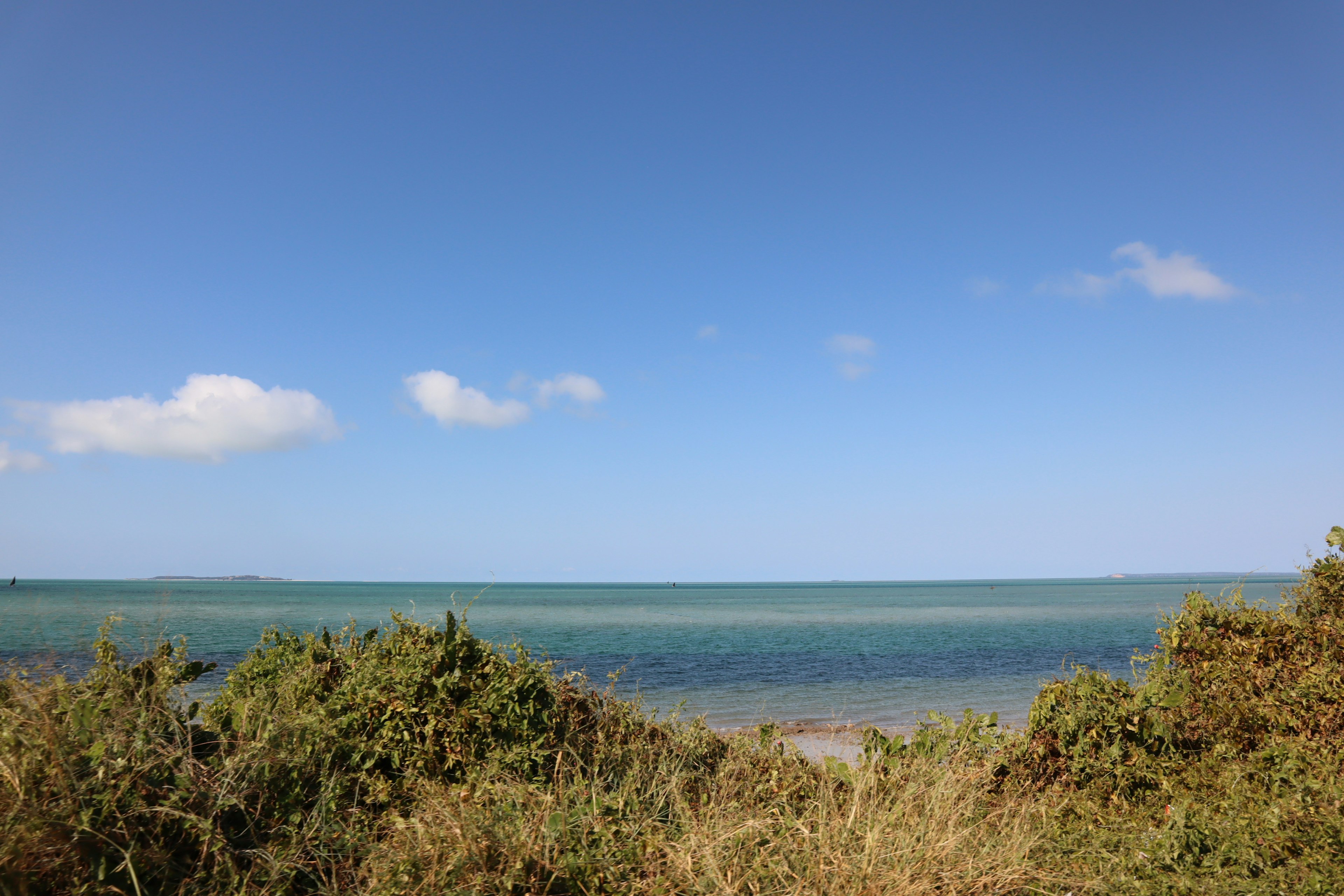 Un paysage naturel avec une mer et un ciel bleus, une côte et de la végétation visibles