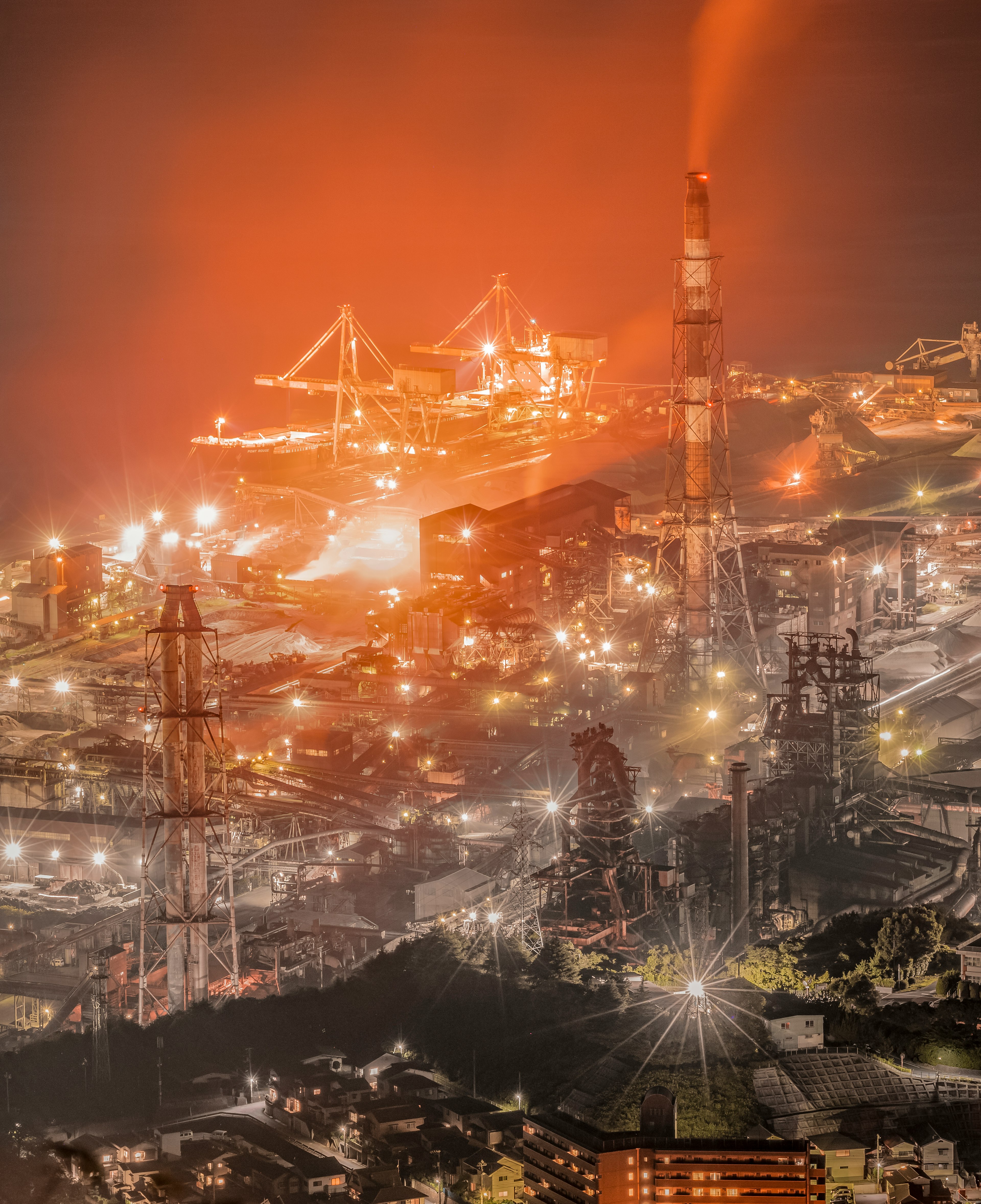 Industrial area at night with glowing lights and prominent smokestacks