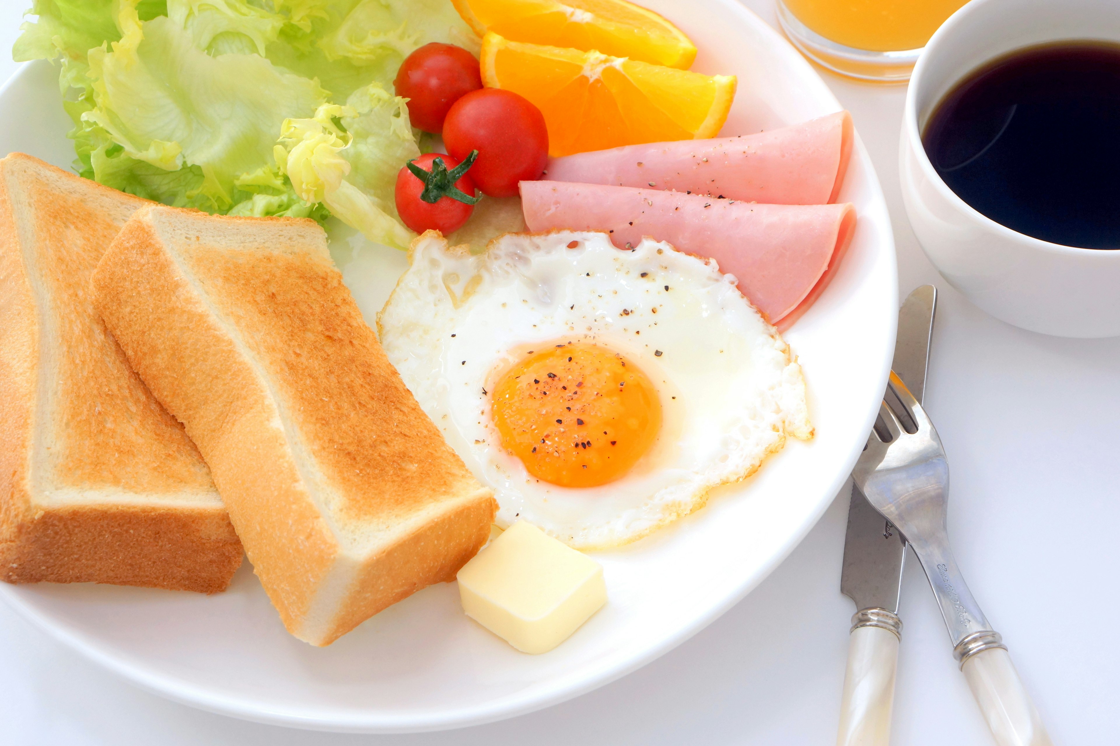 Piatto per la colazione con toast, uovo fritto, lattuga, pomodori, arancia e prosciutto