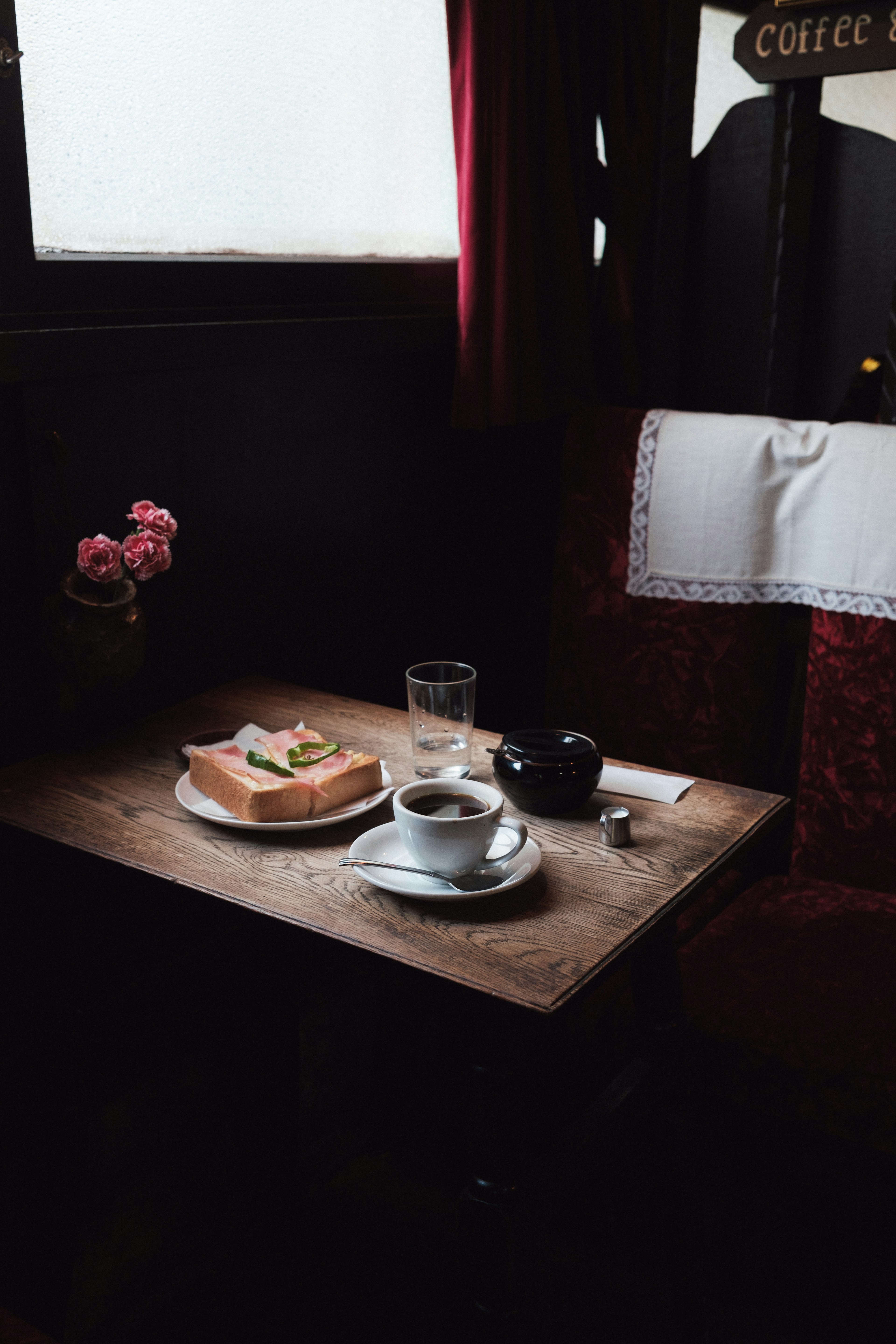 Una mesa de madera con tostadas y café Luz suave que entra por la ventana Cortinas rojas y un jarrón con flores presentes