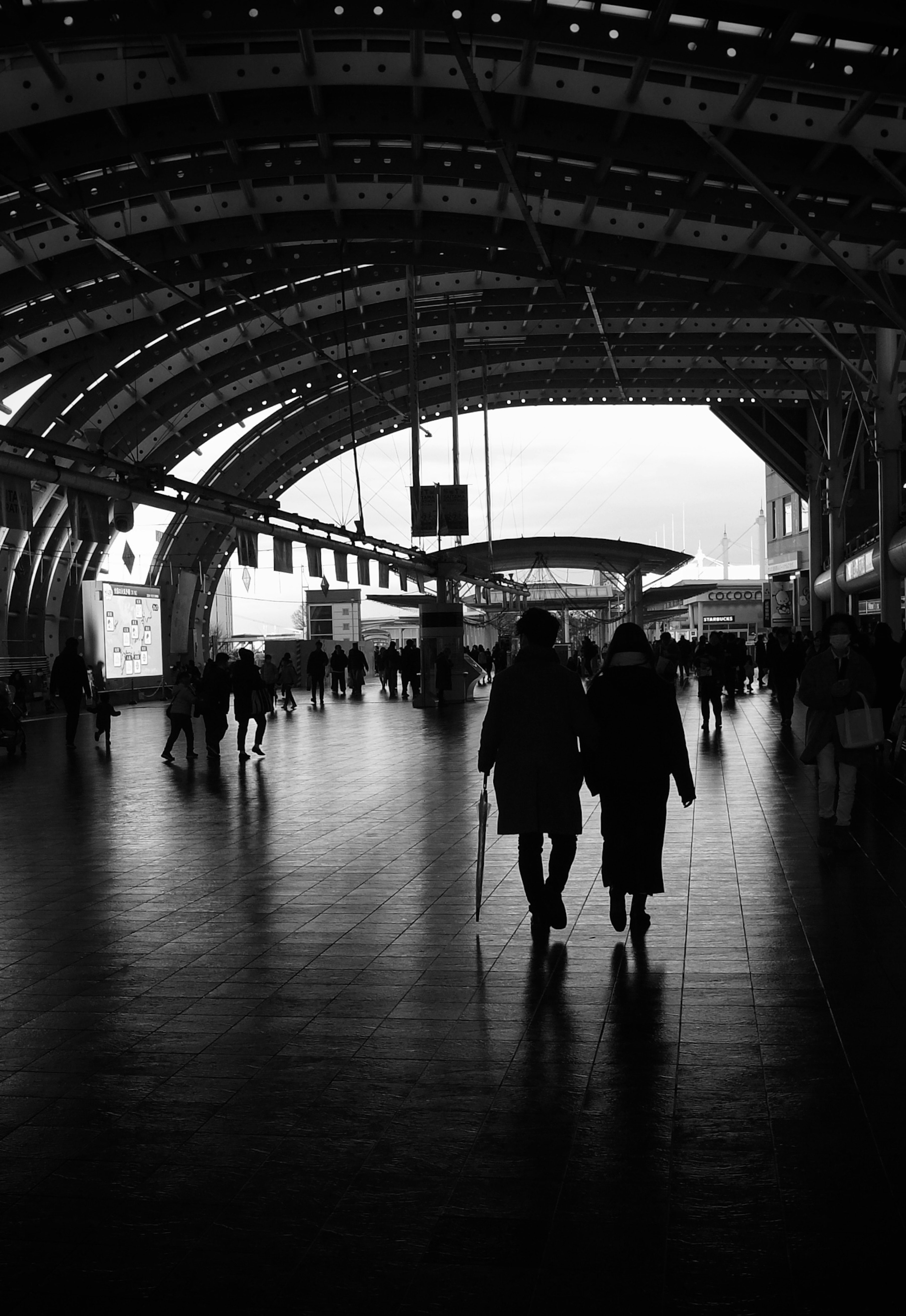 Silhouette of people walking inside a train station with a modern arched roof