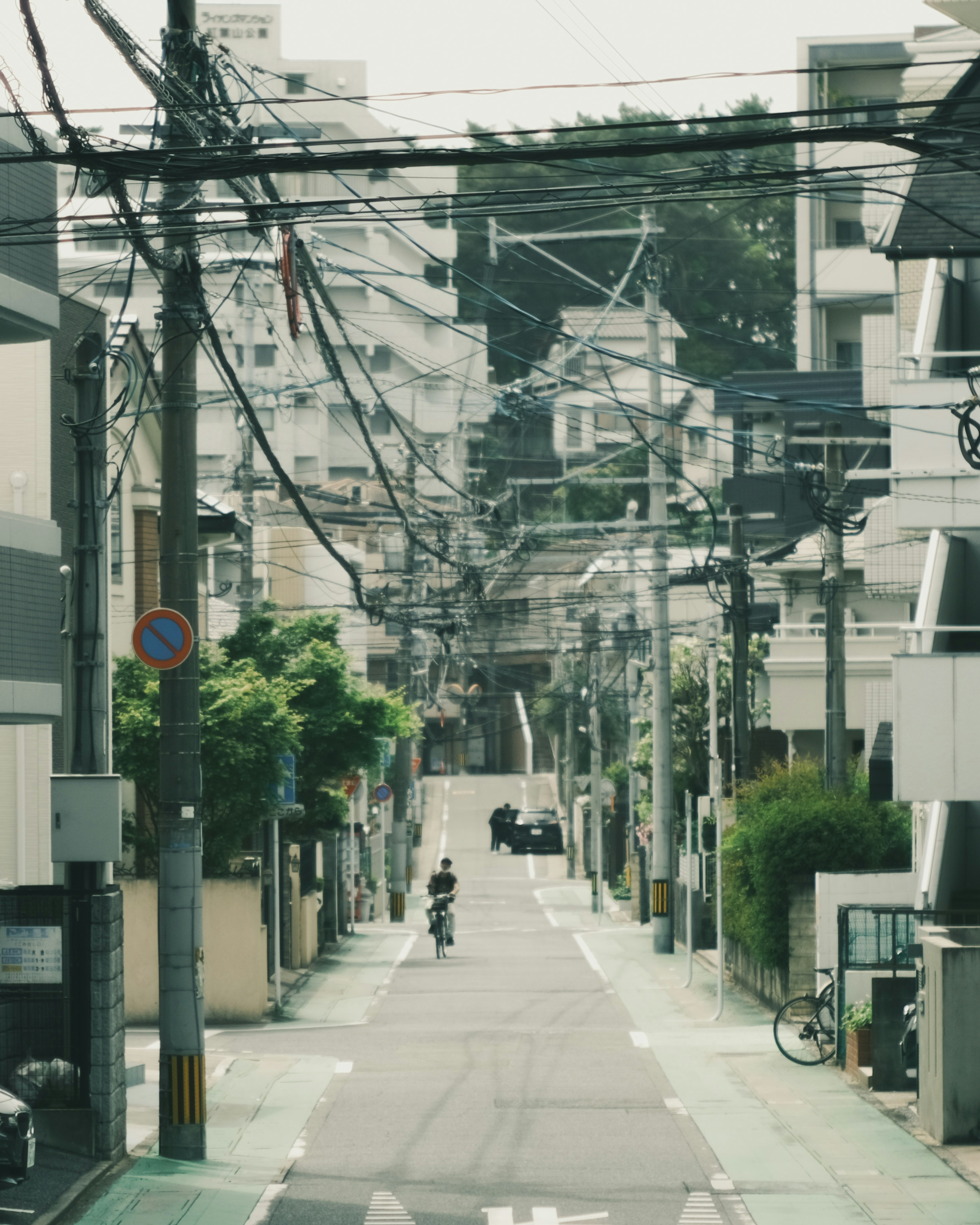 Narrow street view of a residential area with power lines and a cyclist