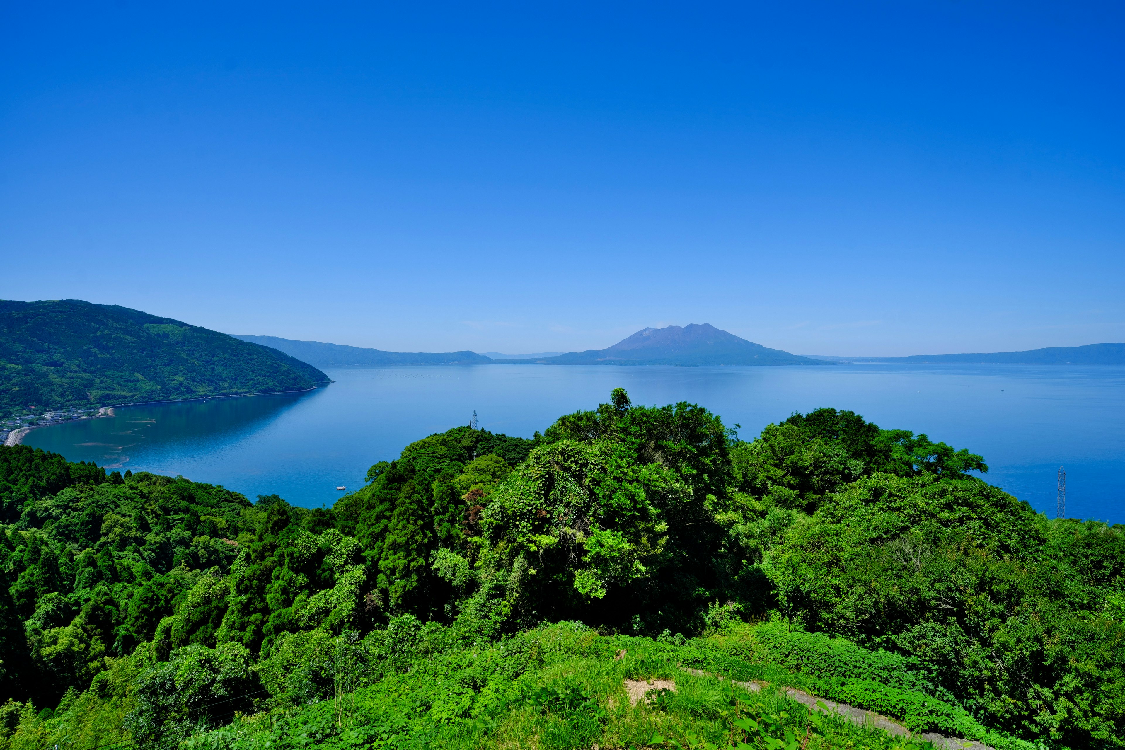 Vista escénica de una colina verde exuberante que domina un lago tranquilo bajo un cielo azul claro