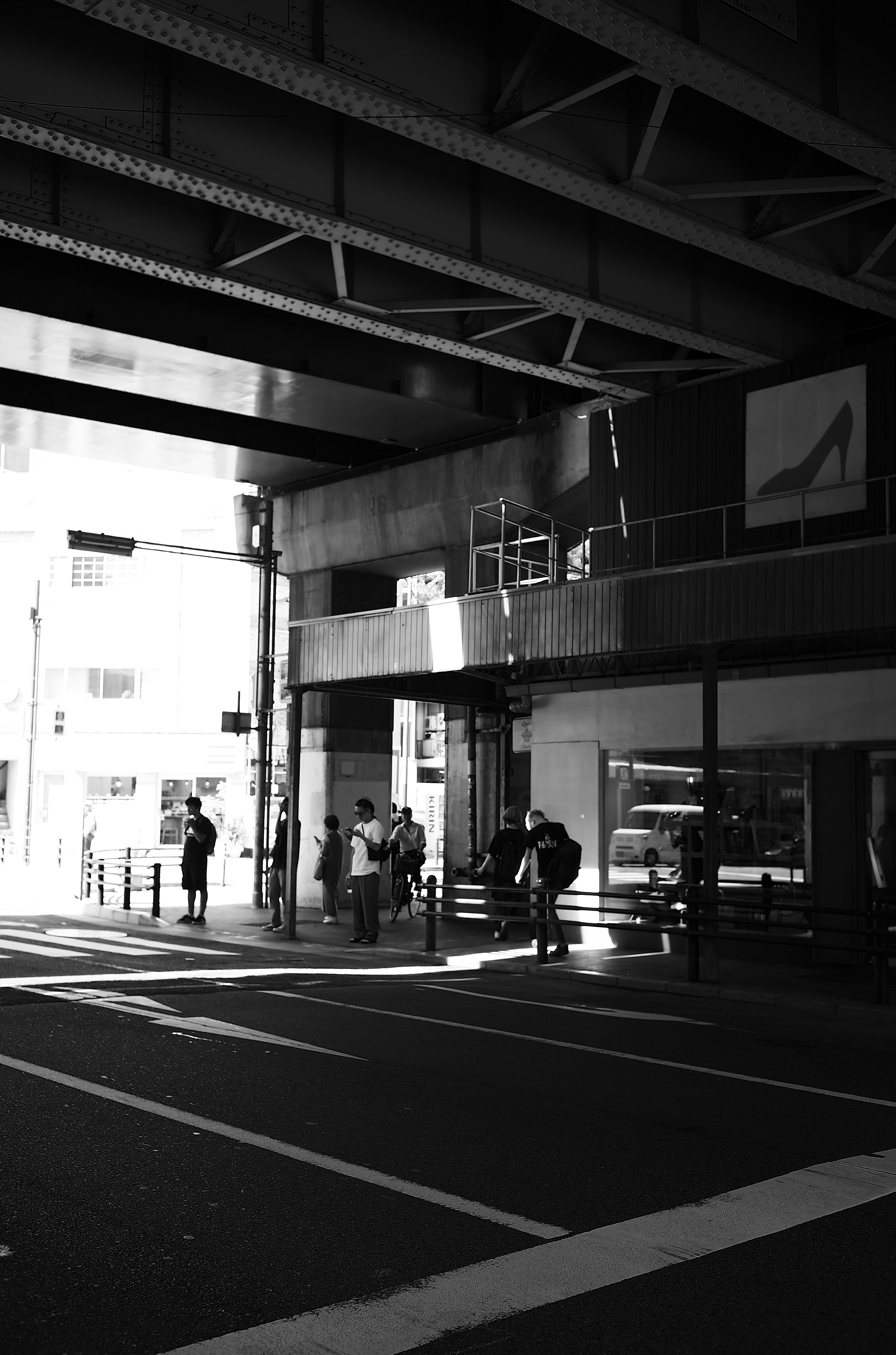 Scène urbaine en noir et blanc avec des personnes marchant sous un viaduc