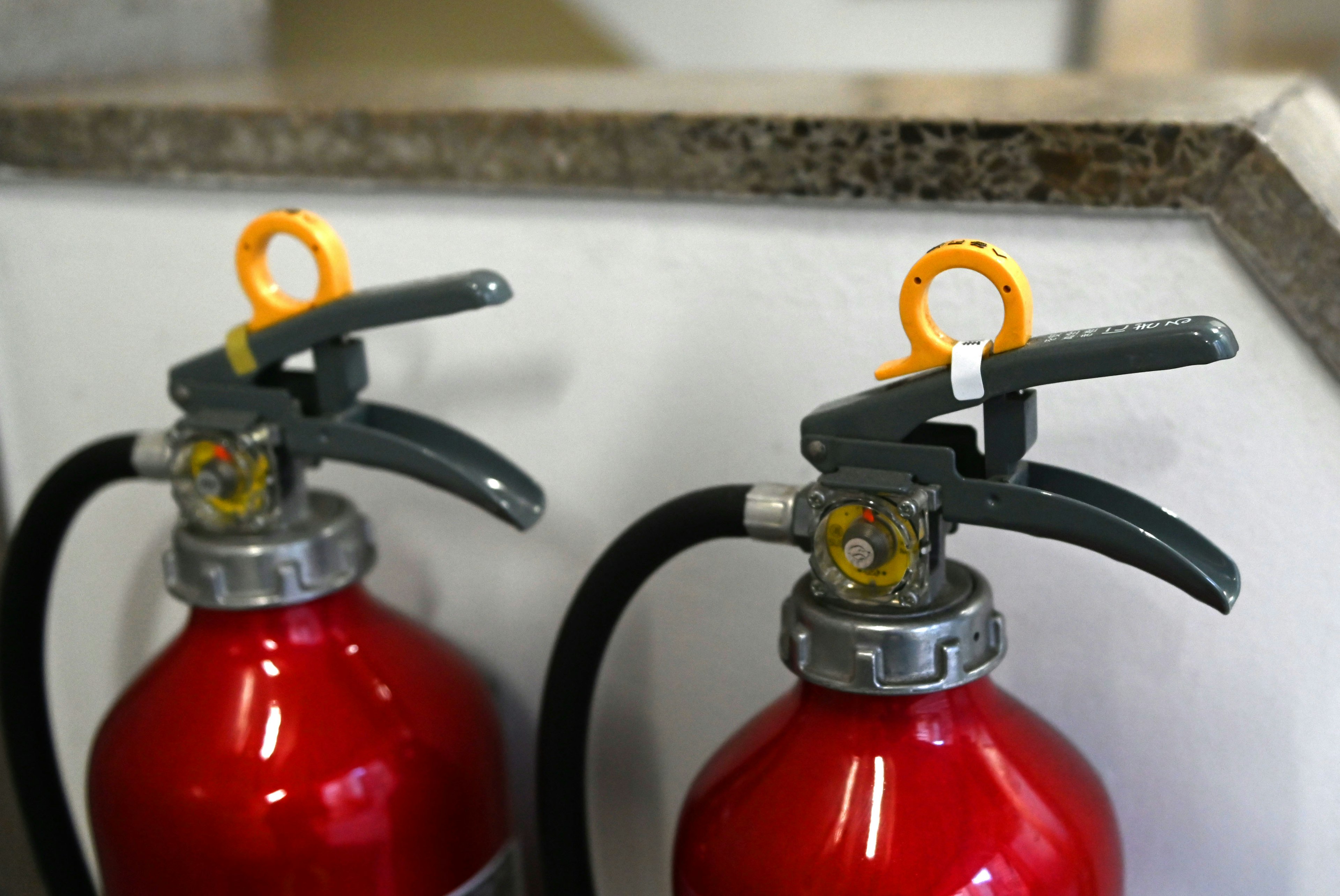 Two red fire extinguishers with gray handles and orange pins on a granite surface