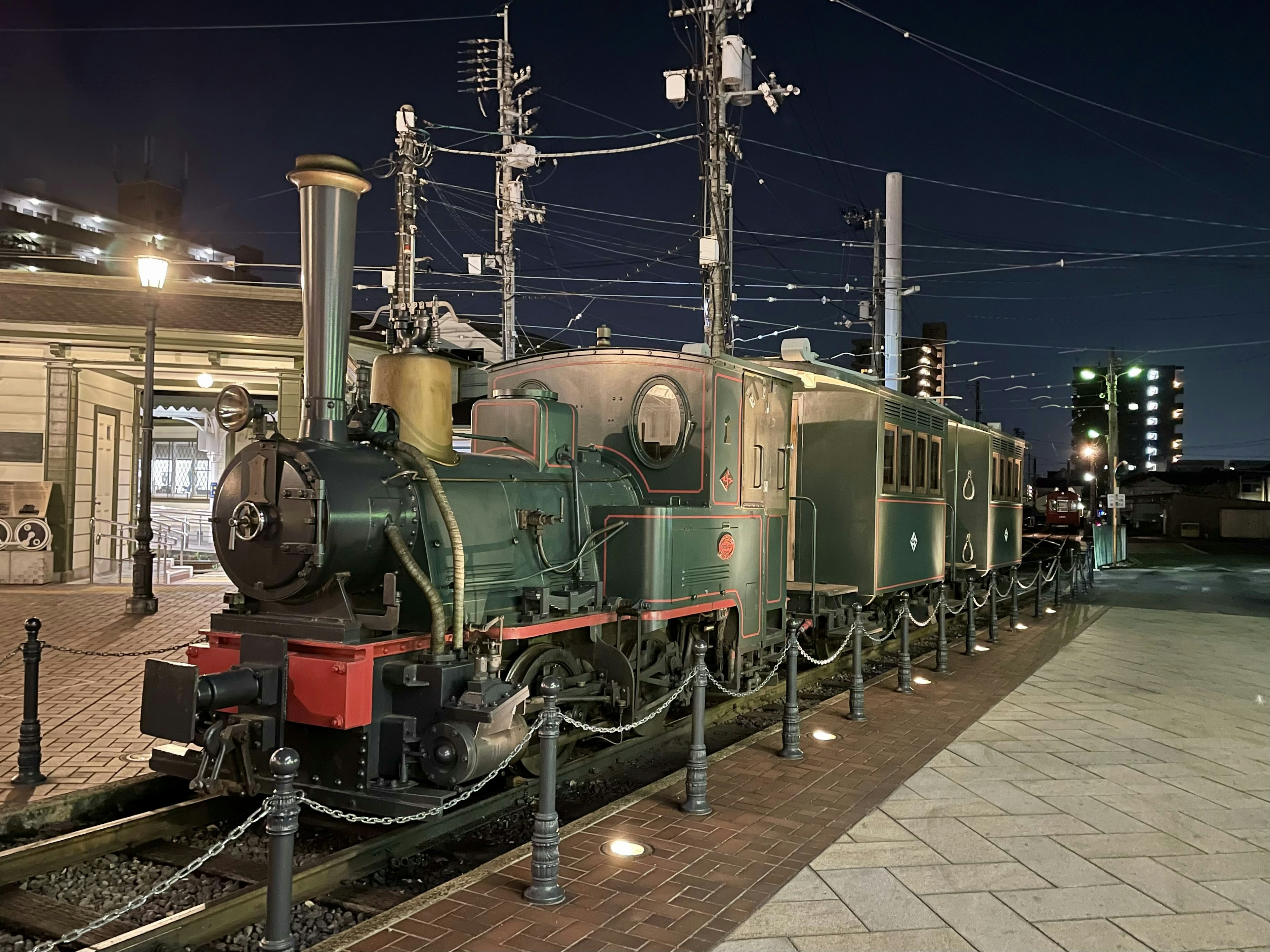 Green steam locomotive and passenger car parked at night station