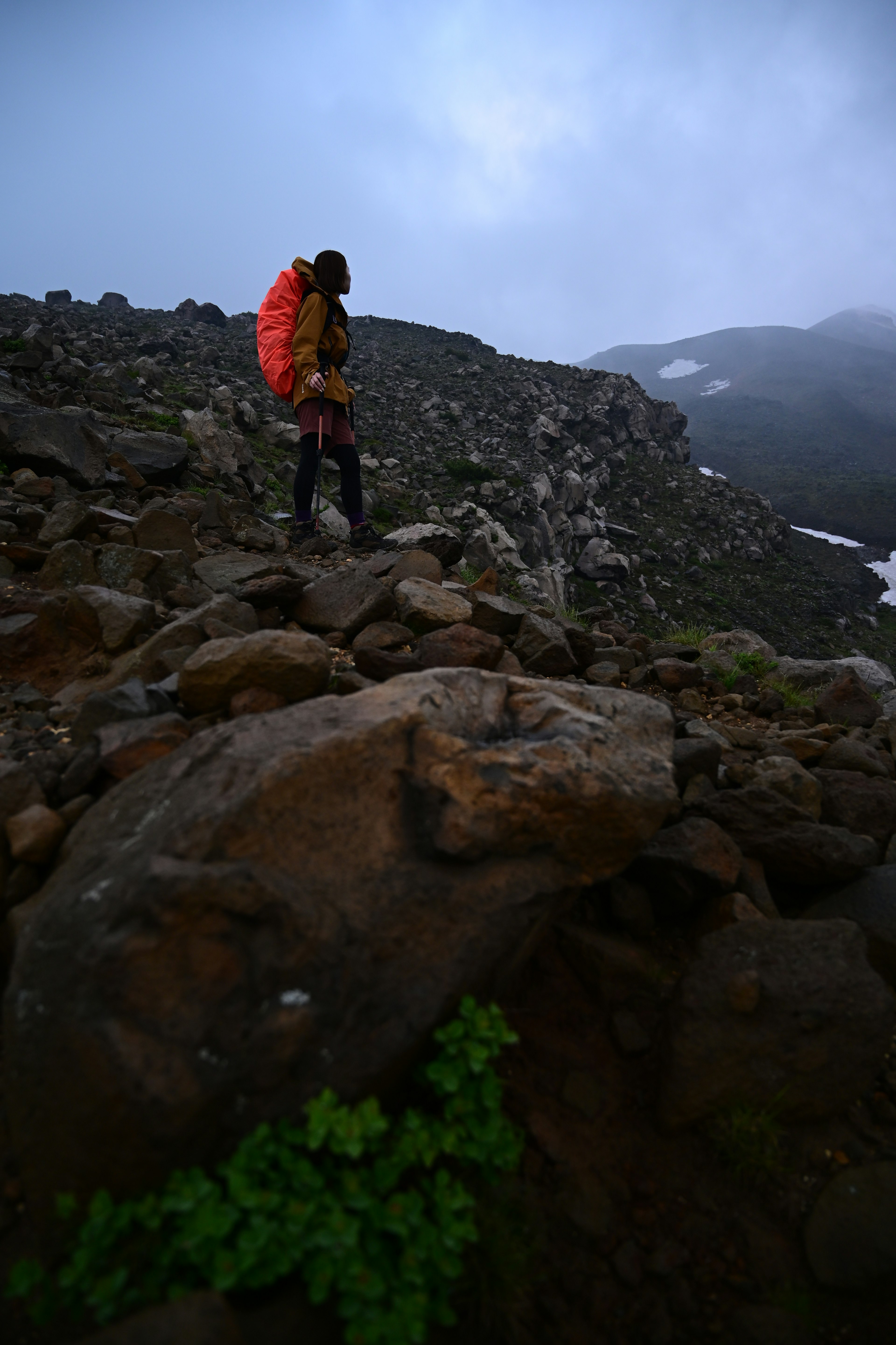 Hiker standing on rocks with an orange backpack in a misty mountainous landscape